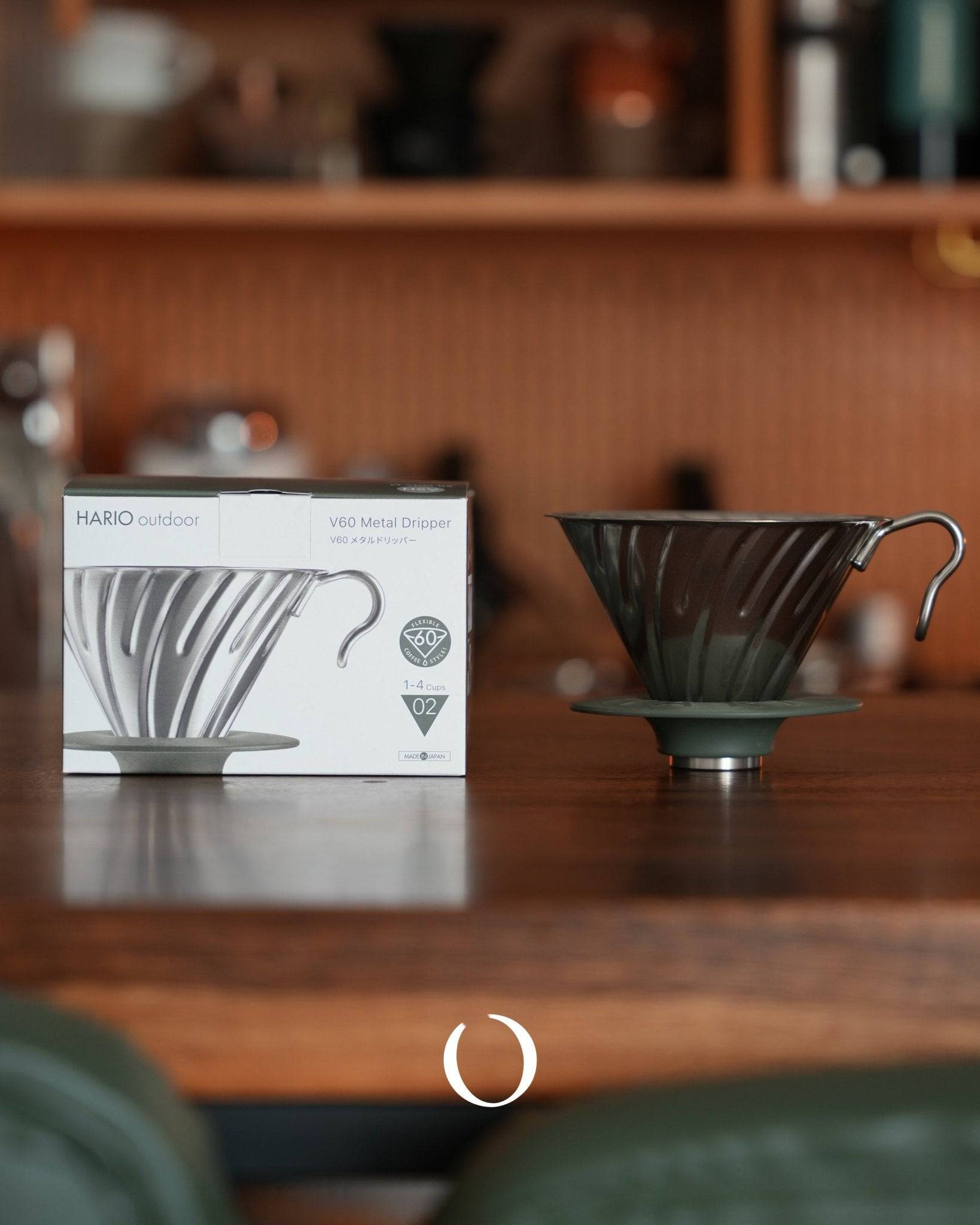HARIO V60 02 stainless steel metal dripper in silver color displayed on wooden surface with product box, showcasing conical design and spiral ribs for optimal coffee extraction