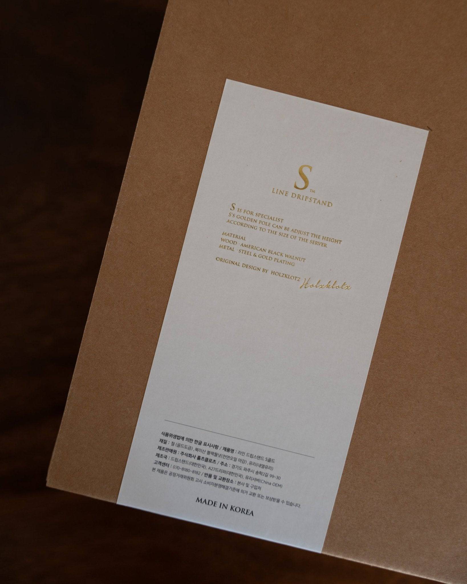 Elegant white card with gold lettering displaying product information for Holzklotz coffee set, placed on brown background, showcasing premium branding and Korean origin