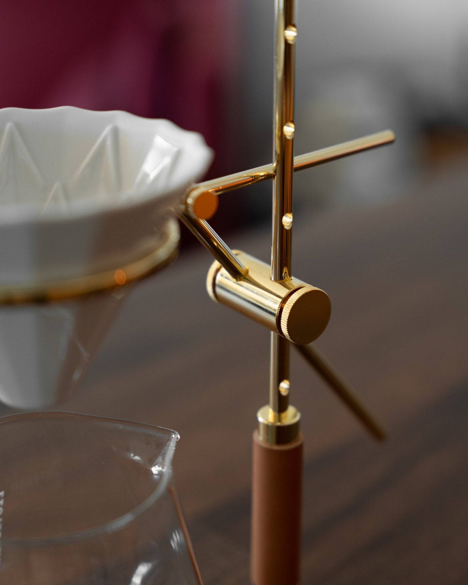 Elegant gold-plated pour-over coffee stand with adjustable arms holding a white ceramic dripper, showcasing Holzklotz&