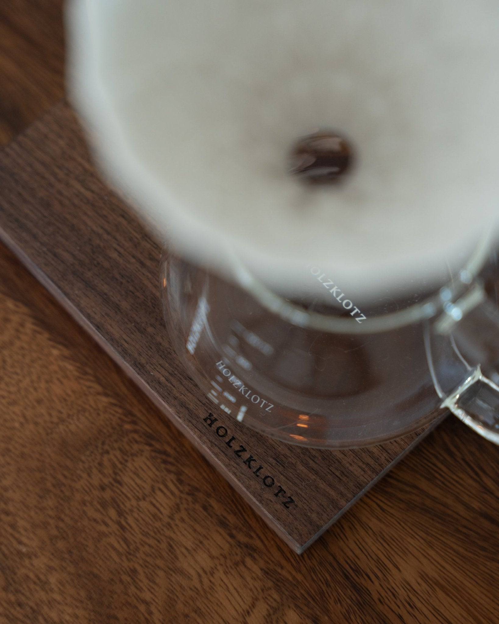 Close-up of Holzklotz coffee dripper set featuring white ceramic filter, glass carafe, and wooden base, showcasing elegant design and premium materials for pour-over coffee brewing