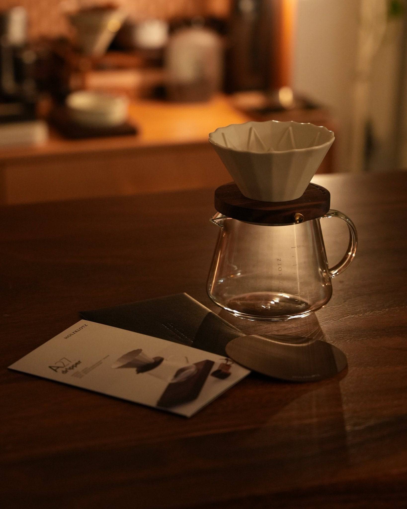 Holzklotz pour-over coffee set on wooden table featuring A27 filter, black walnut holder, and glass carafe, with product brochure in warm, ambient lighting