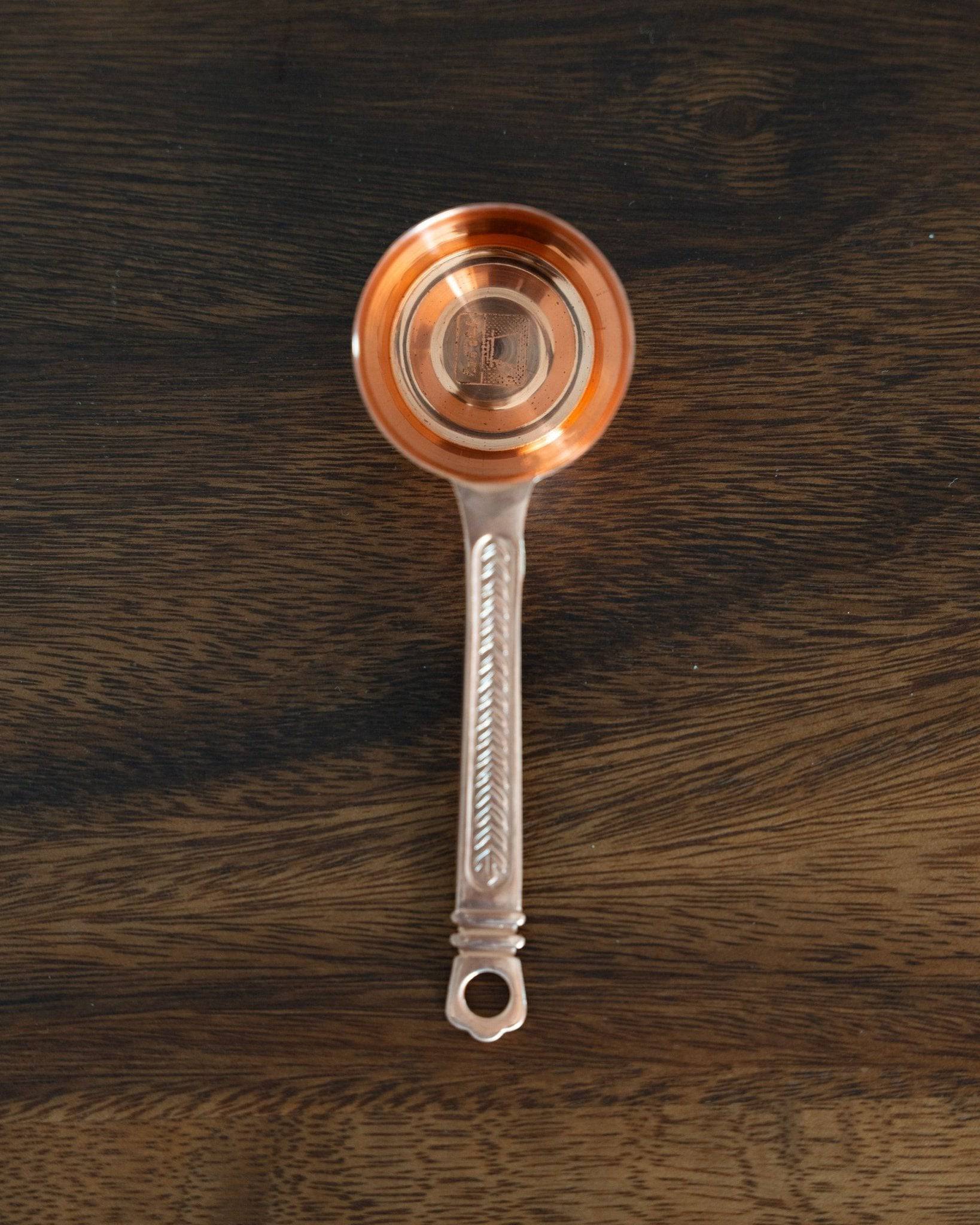 Elegant copper Kalita coffee scoop with laurel wreath pattern, 10g capacity, long textured handle, on dark wood background