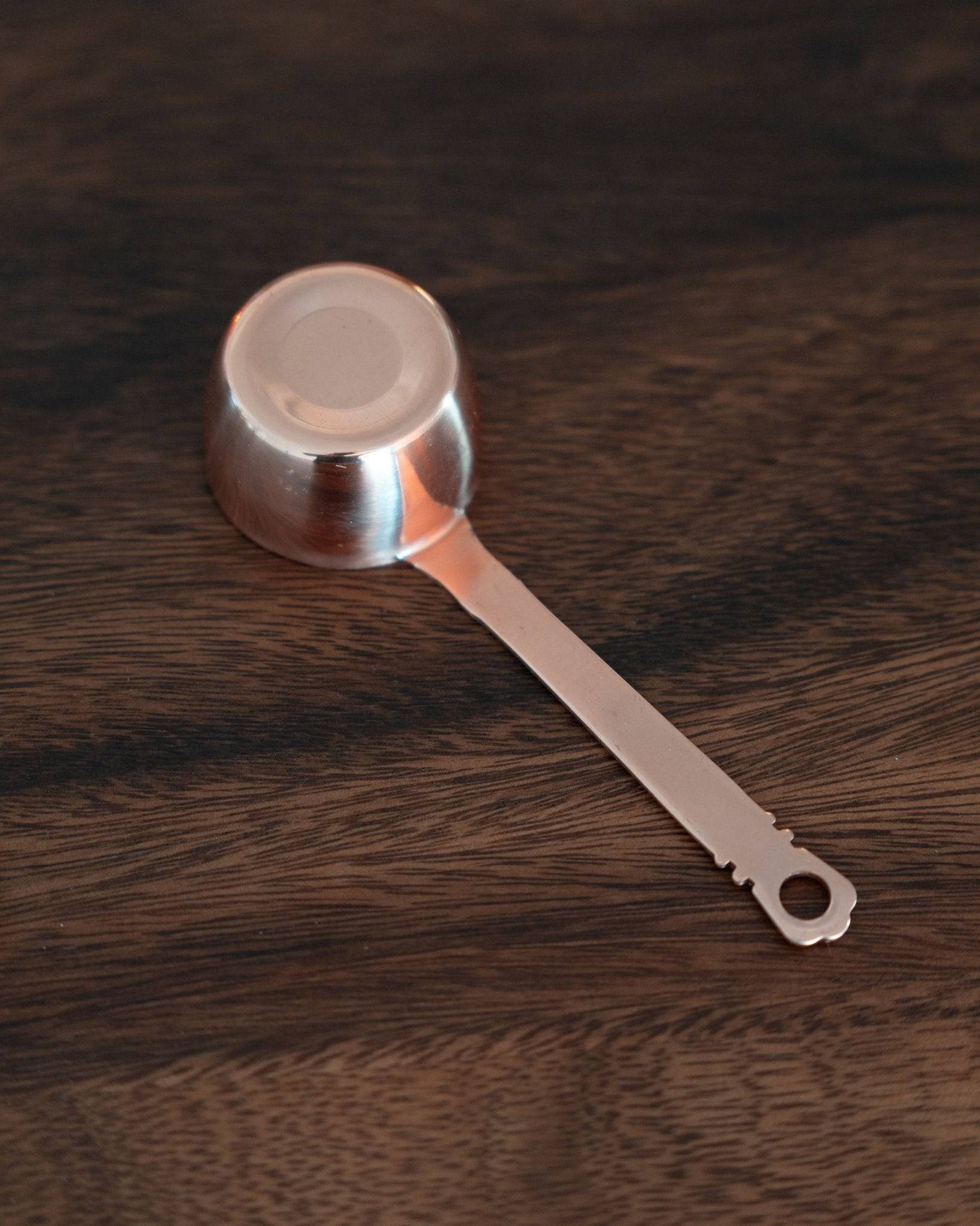 Elegant copper coffee scoop with laurel wreath pattern handle, 10g capacity, on dark wooden surface. Kalita brand precision measuring tool for coffee beans.