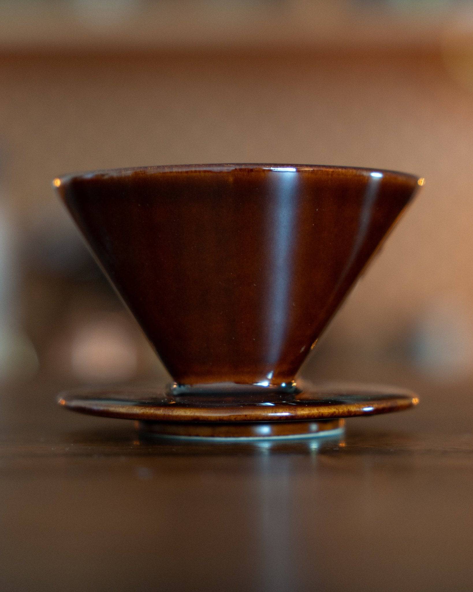 Kalita 101 ceramic coffee dripper in brown, showcasing its conical shape and glossy finish, placed on a wooden surface, highlighting its Japanese craftsmanship and functionality for pour-over coffee brewing.