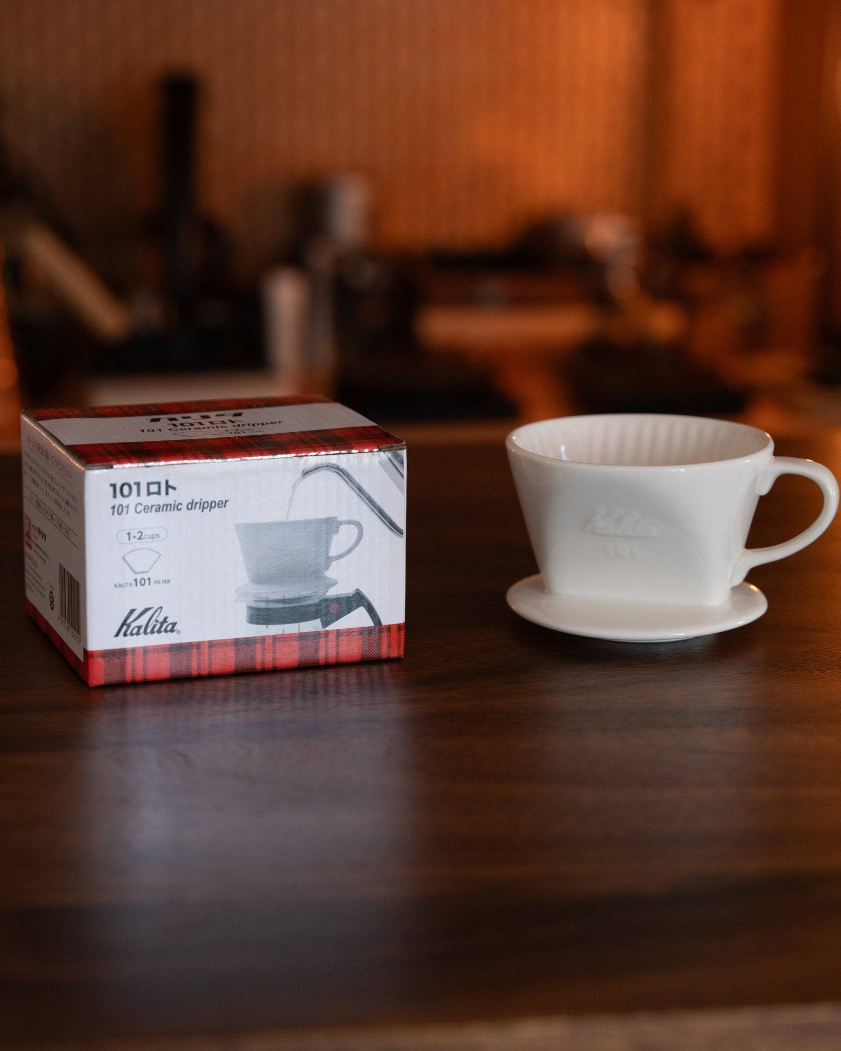 Kalita 101 ceramic dripper in white, displayed with product box on wooden surface, showcasing Japanese craftsmanship for pour-over coffee brewing