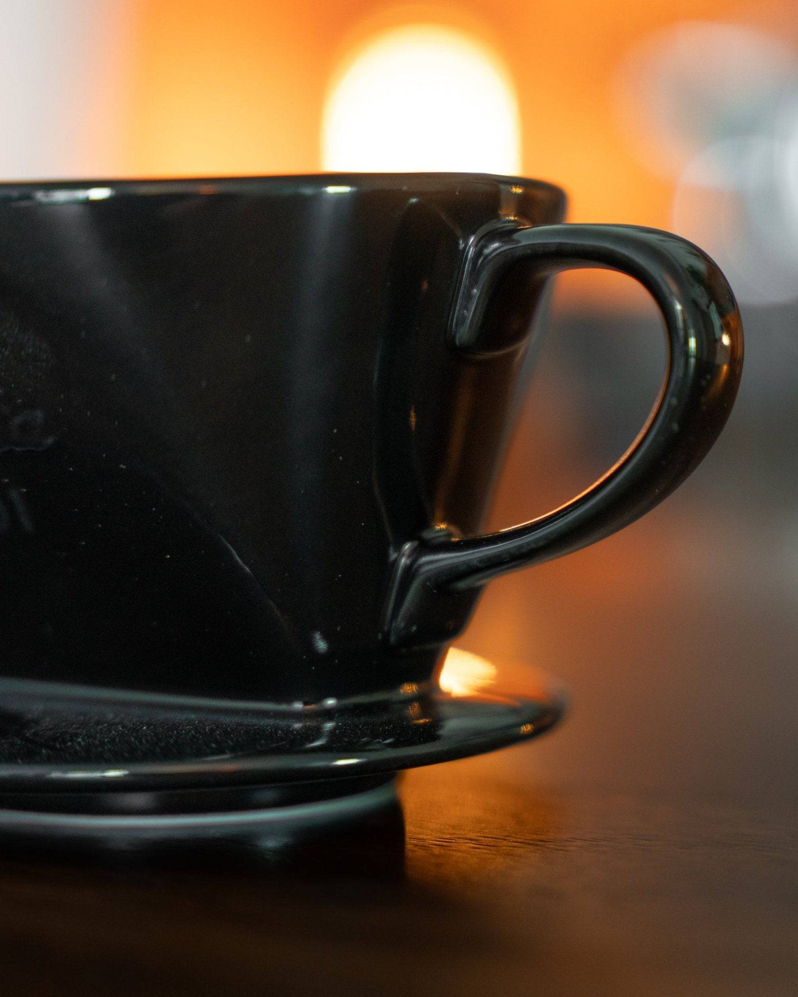 Black Kalita ceramic pour-over coffee dripper on wooden surface with warm backlight, showcasing its sleek design and high-quality Japanese craftsmanship for optimal coffee brewing