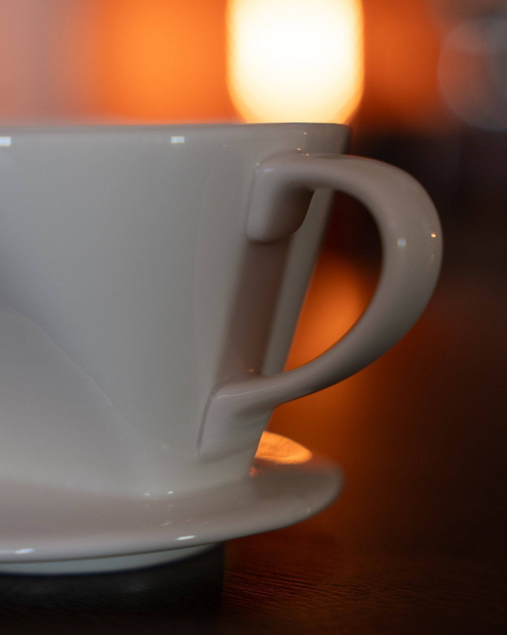 Close-up of a white ceramic Kalita pour-over coffee dripper with distinctive handle and base, illuminated by warm ambient lighting, showcasing its elegant design and quality craftsmanship for brewing premium coffee