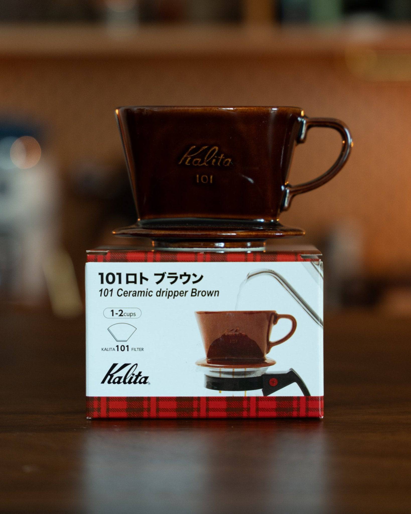 Kalita 101 ceramic coffee dripper in brown, displayed on its product box. Japanese-made pour-over coffee filter with unique design, suitable for 1-2 cups, showcasing high-quality craftsmanship and elegant appearance.