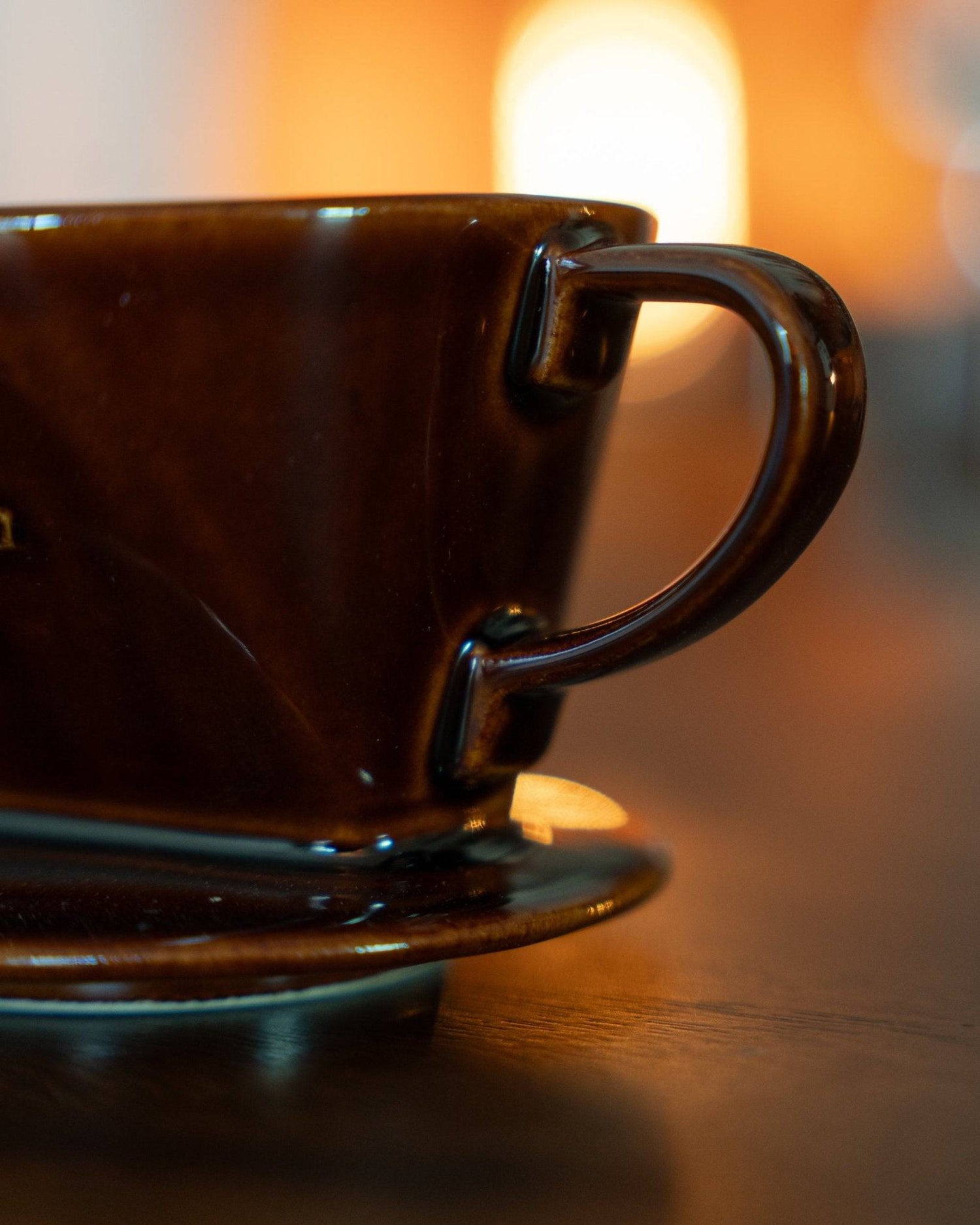 Close-up of Kalita brown ceramic pour-over coffee dripper on wooden surface with warm backlighting, showcasing its elegant design and craftsmanship for premium home brewing