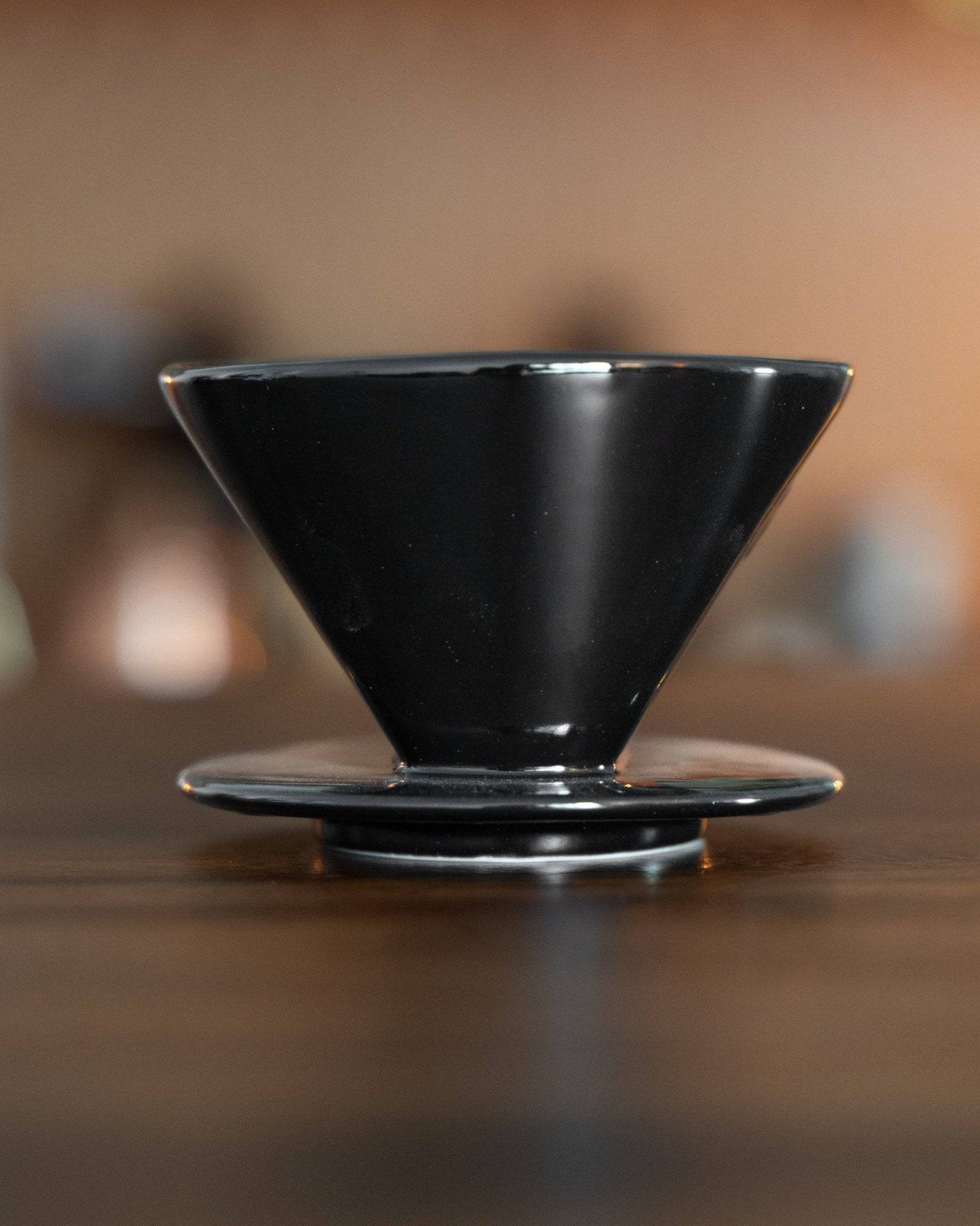 Kalita 101 black ceramic coffee dripper on wooden surface, conical shape with wide rim and narrow base, showcasing sleek design and quality craftsmanship for pour-over brewing