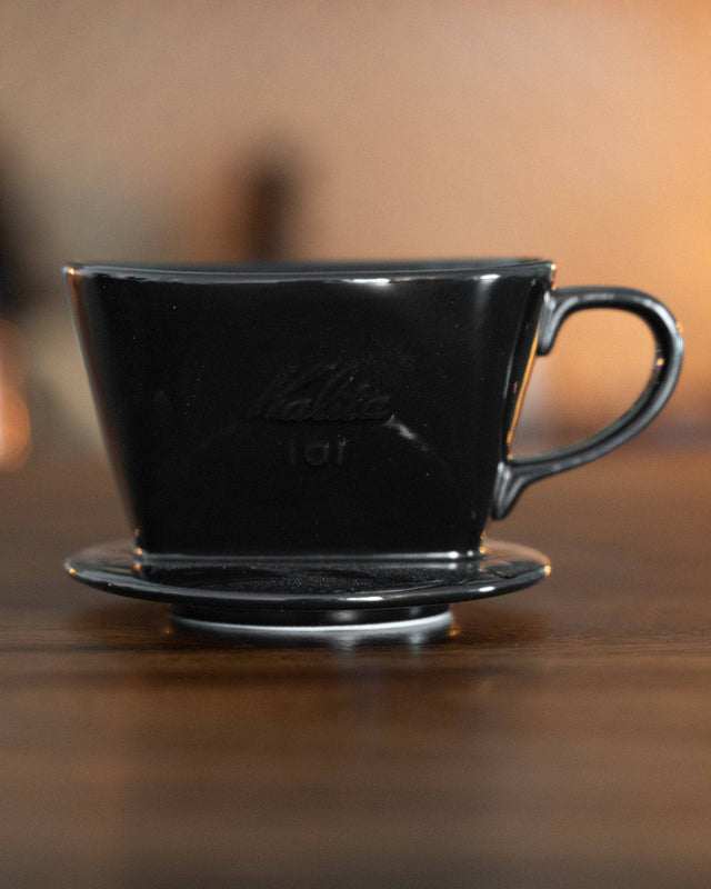 Kalita 101 black ceramic pour-over coffee dripper on wooden surface, showcasing its unique trapezoidal shape and glossy finish, ideal for brewing 1-2 cups of coffee