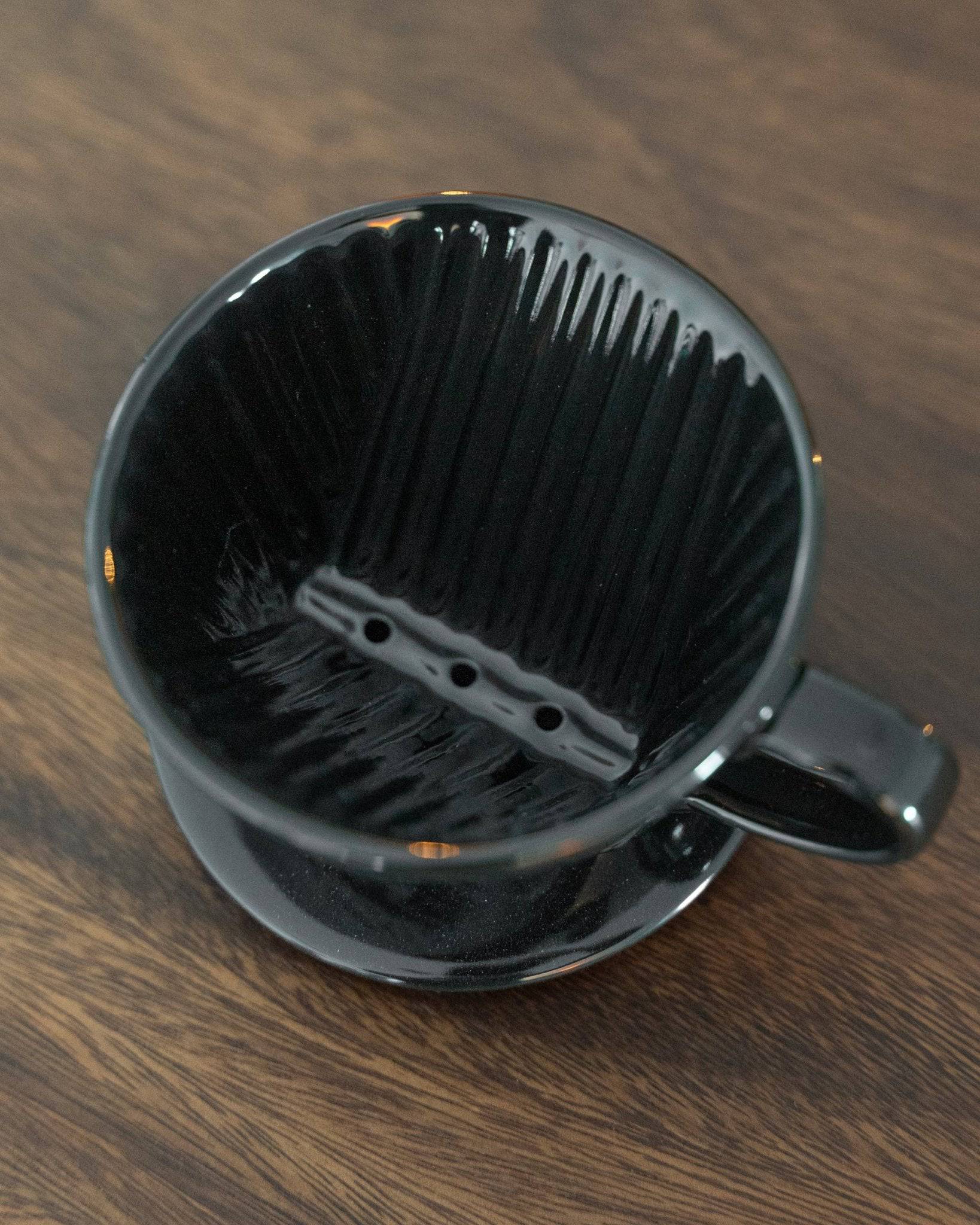 Kalita 101 black ceramic coffee dripper with distinctive ridged interior design, showcasing unique trapezoid shape and three-hole bottom on wooden surface