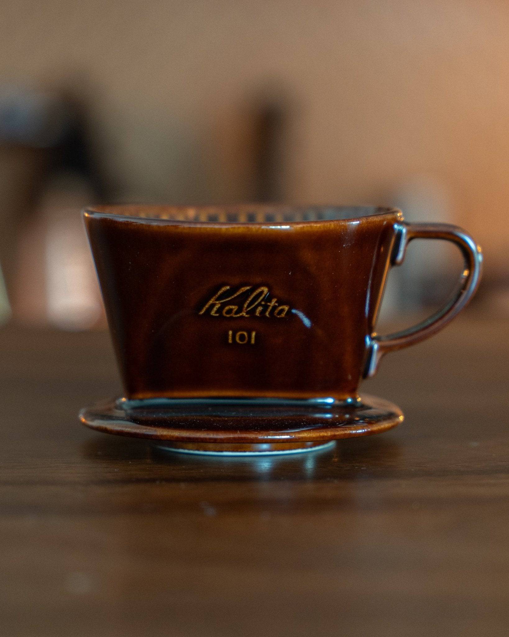 Kalita 101 brown ceramic pour-over coffee dripper on saucer, displaying unique trapezoidal design with visible ridges, showcasing Japanese craftsmanship and quality for premium home brewing experience