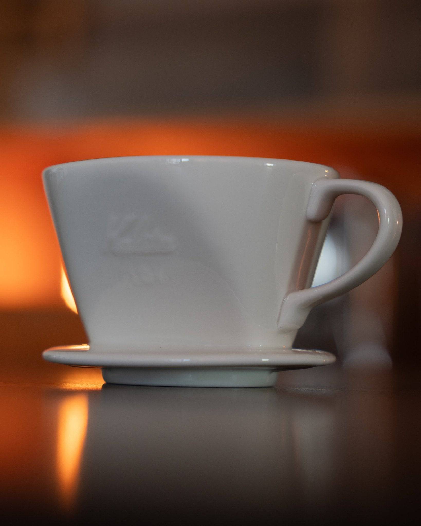 Kalita classic white ceramic pour-over coffee dripper with conical shape and textured exterior, displayed on reflective surface with warm ambient lighting