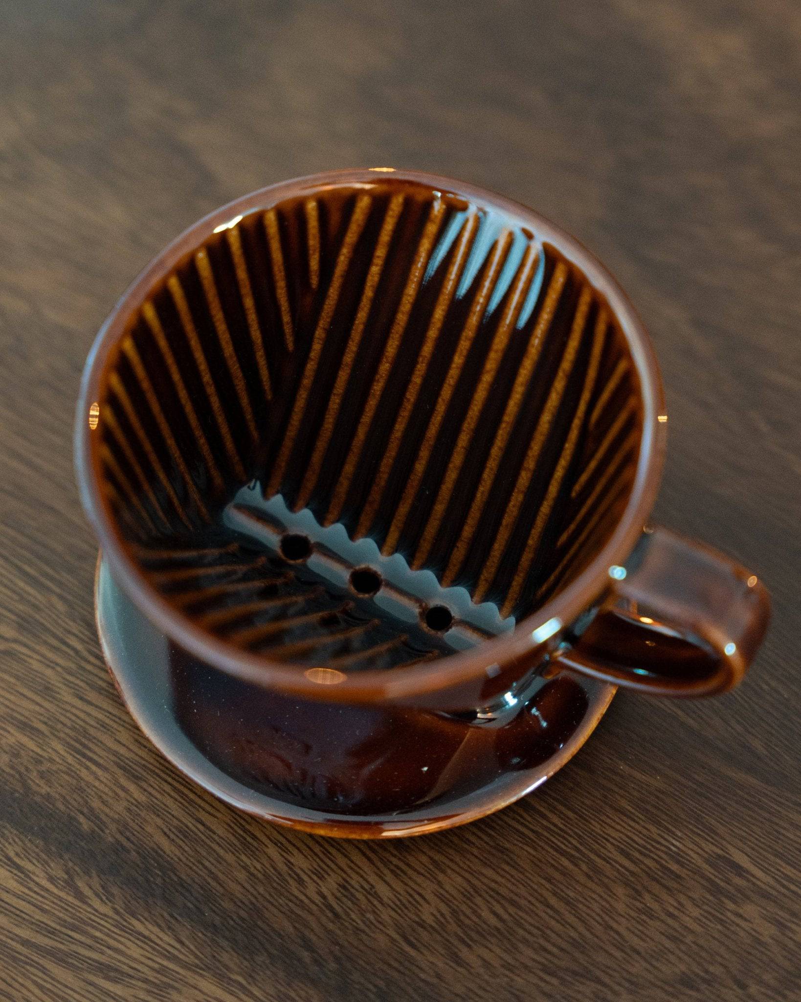 Kalita 101 brown ceramic coffee dripper with unique ribbed interior design, showcasing its distinctive conical shape and three-hole bottom on a wooden surface