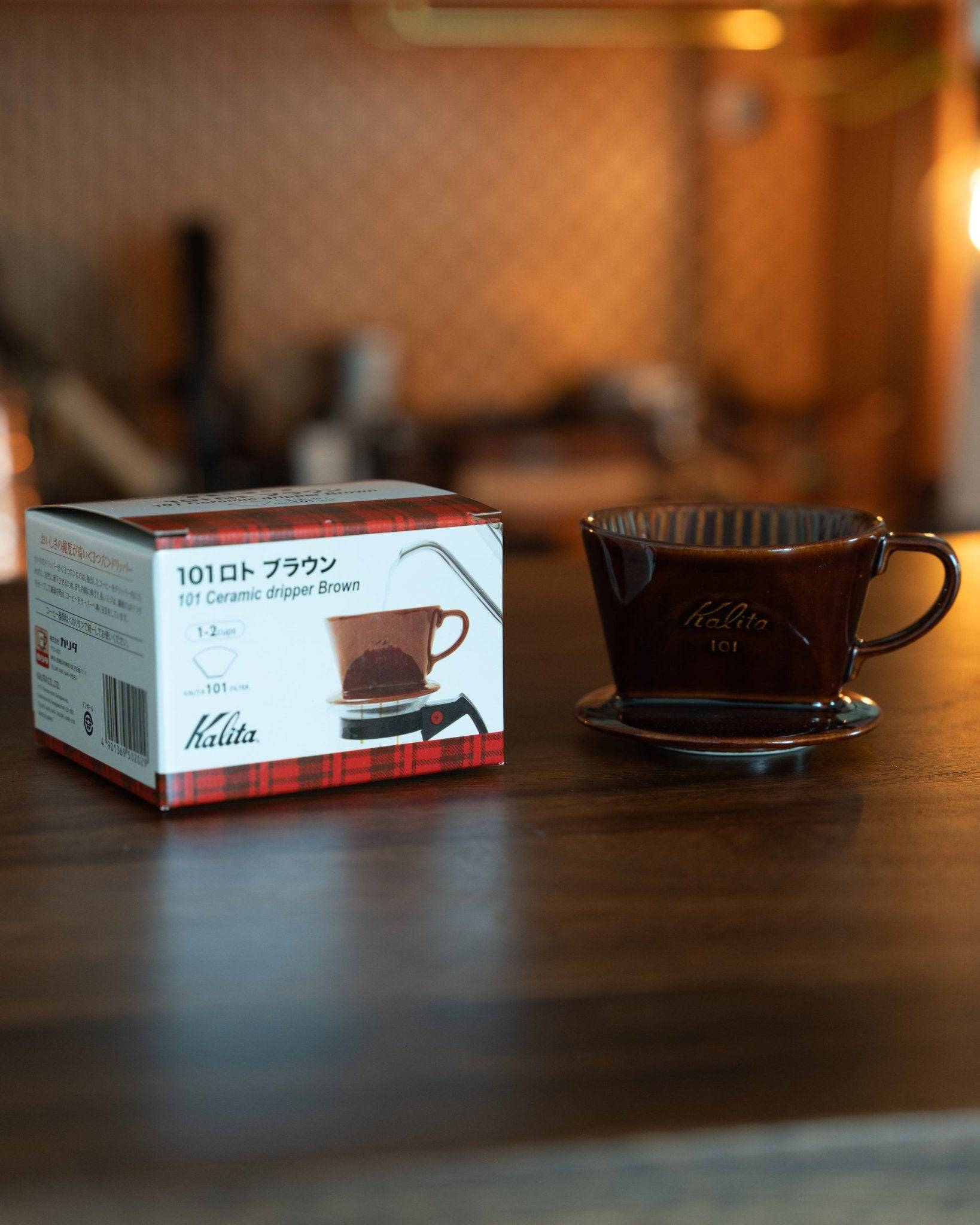 Kalita 101 ceramic coffee dripper in brown, displayed with its product box on a wooden surface, showcasing Japanese craftsmanship and design for pour-over coffee brewing