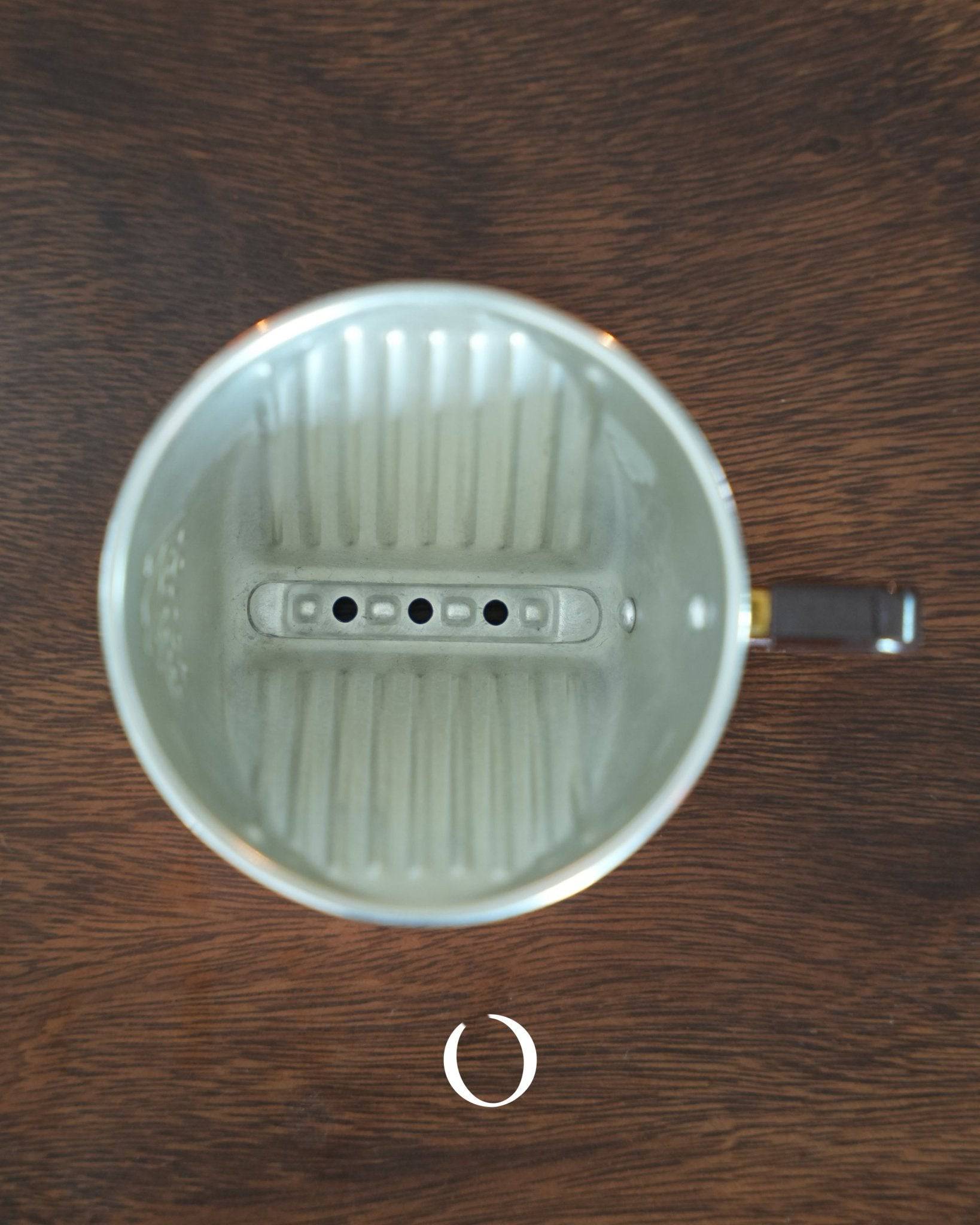KALITA copper coffee dripper with three-hole design, showcasing its interior ribbed structure and unique bottom holes, placed on a dark wooden surface