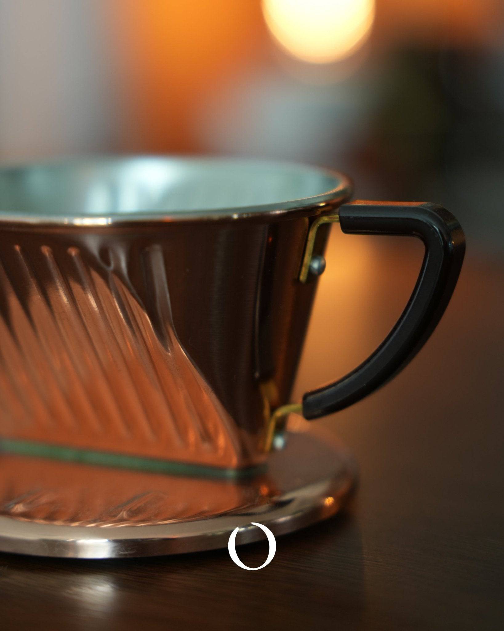 Copper KALITA pour-over coffee dripper with ribbed design and black handle, reflecting warm light, showcasing its premium craftsmanship and heat conductivity for optimal coffee extraction