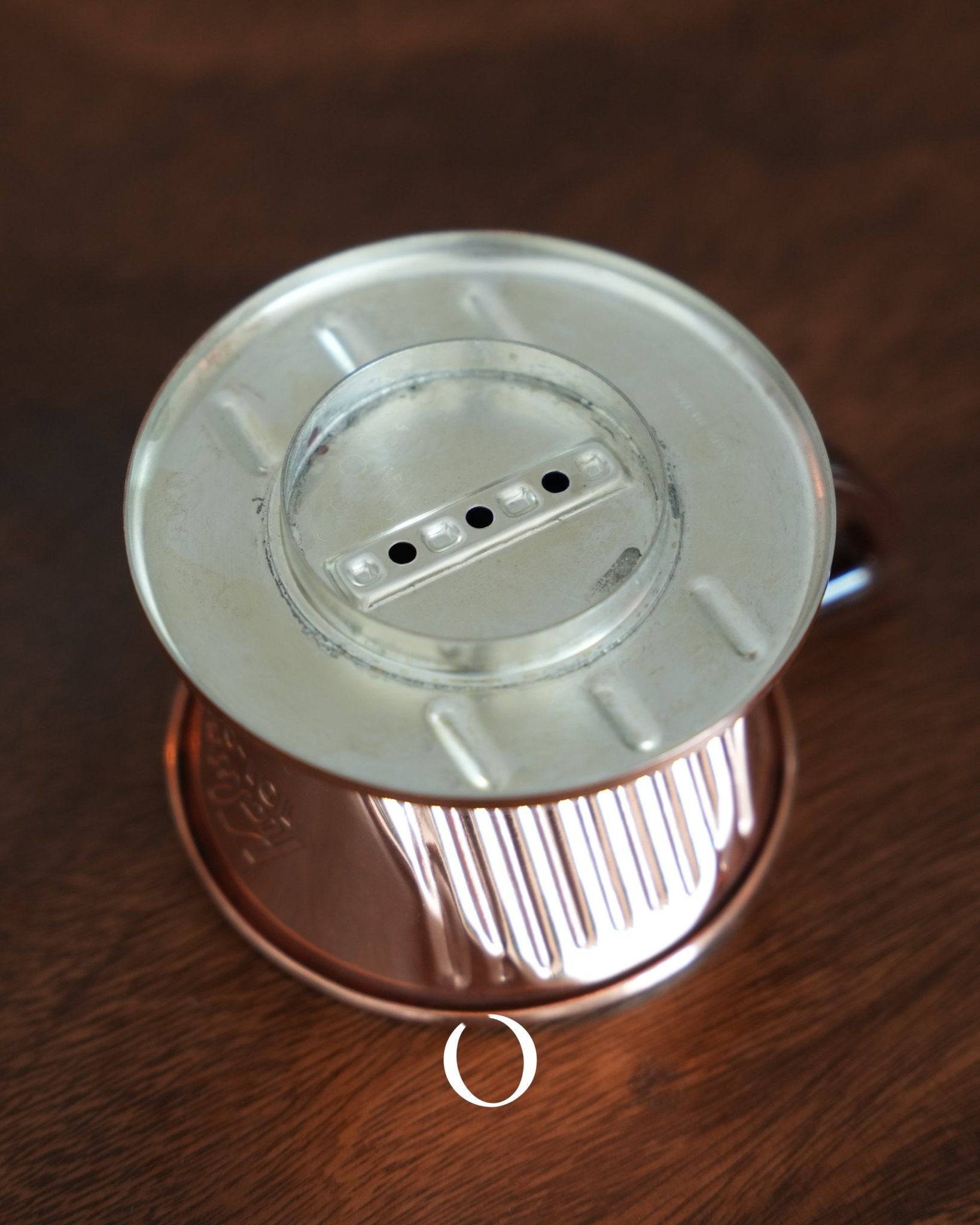 Copper KALITA coffee dripper with three-hole design, featuring a silver top and ribbed copper base, showcasing its unique construction for balanced extraction and heat distribution on a wooden surface