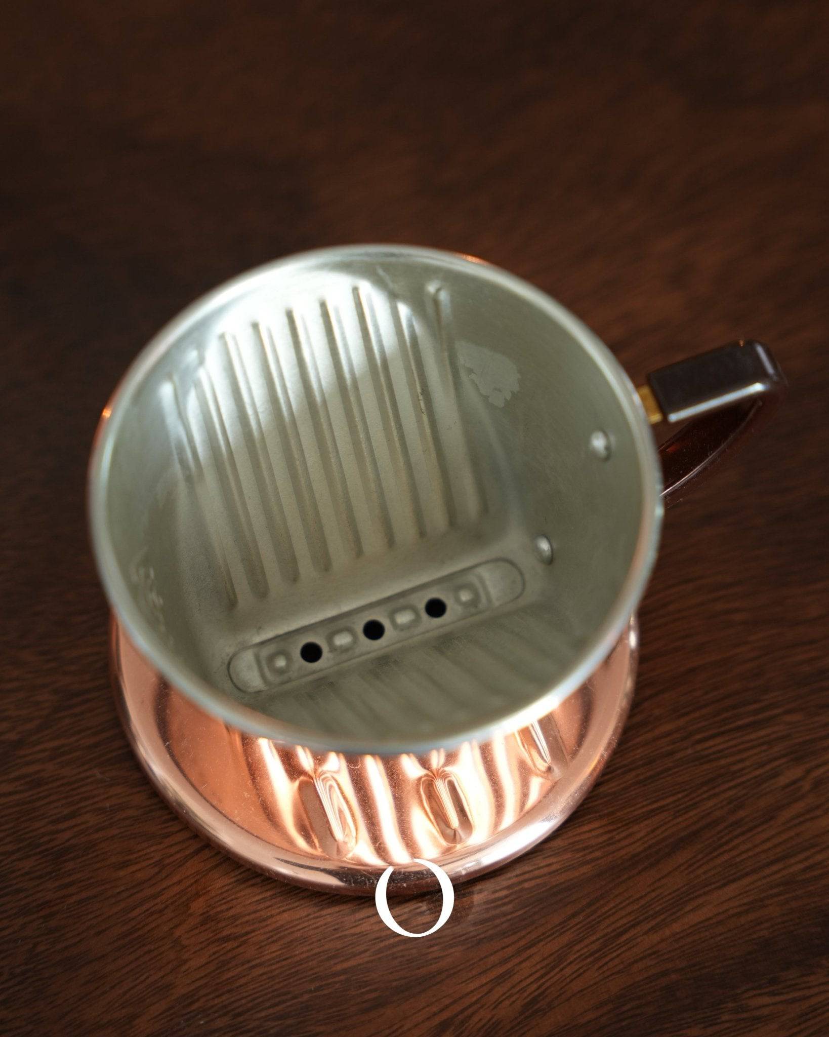 Kalita copper pour-over coffee dripper with three-hole design, viewed from above on wooden surface, showcasing its unique interior and exterior design