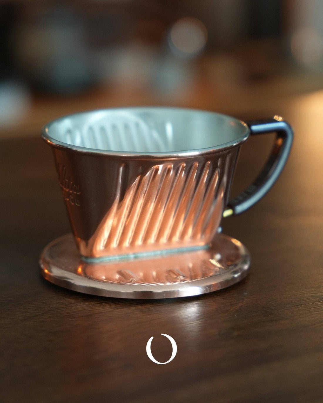 KALITA copper pour-over coffee dripper with three-hole design, featuring a conical shape and ribbed interior, sitting on a metal base, showcasing its handcrafted quality and unique copper finish for optimal heat distribution and balanced extraction