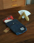 Kalita coffee filter storage bag in denim blue with red plaid lining, displayed next to wooden filter holder and white paper filter on wooden table