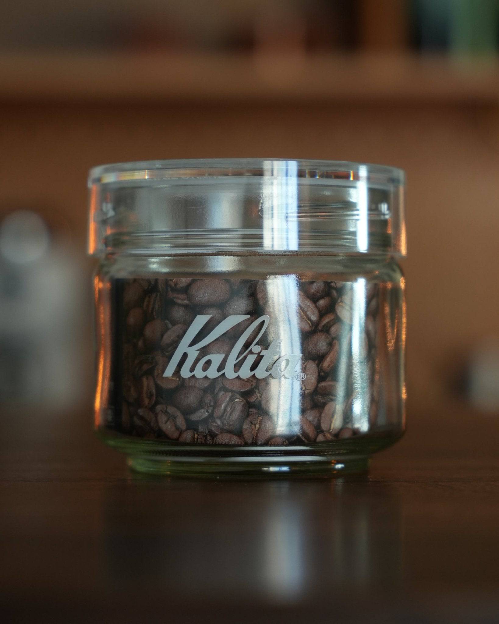Kalita glass coffee canister filled with whole coffee beans, showcasing brand logo and airtight seal, ideal for preserving freshness and aroma