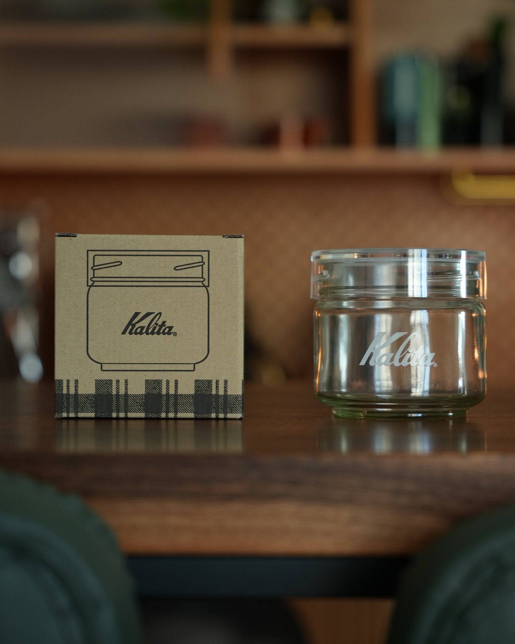Kalita glass coffee storage jar with packaging box on wooden surface, showcasing transparent container with brand logo and cardboard box with jar illustration
