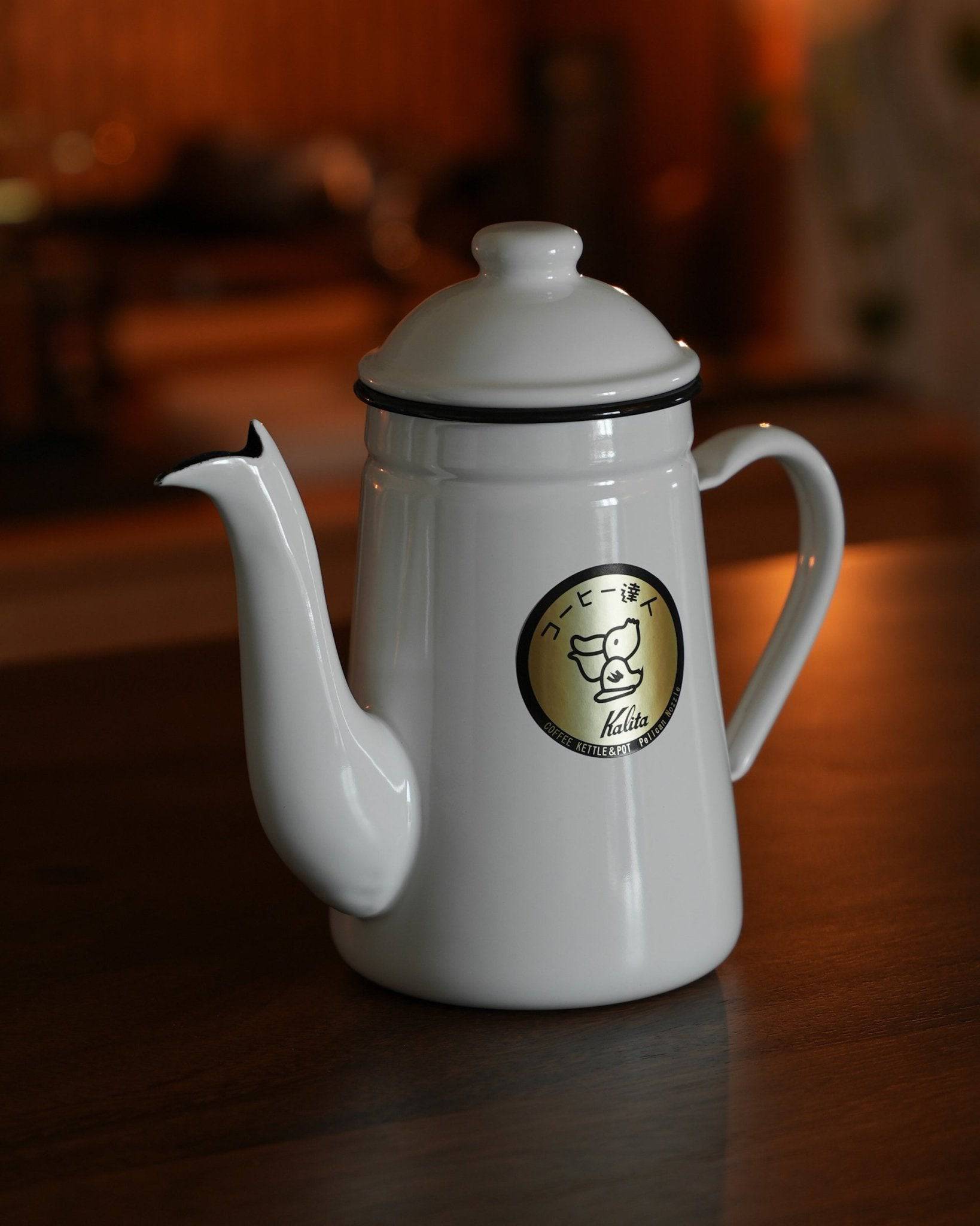 White Kalita enamel kettle with gooseneck spout and Kalita logo on wooden surface, showcasing professional pour-over coffee brewing design and elegant aesthetic