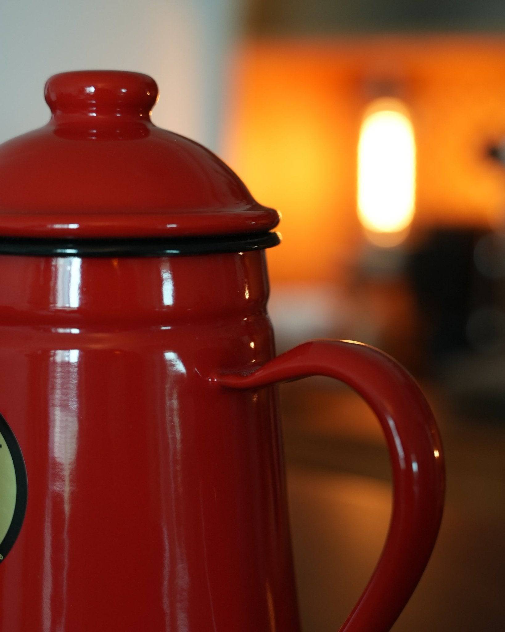 Red enamel Kalita pour-over coffee kettle with curved spout and lid, 1L capacity, shown in warm lighting highlighting its glossy finish and elegant design for precision brewing