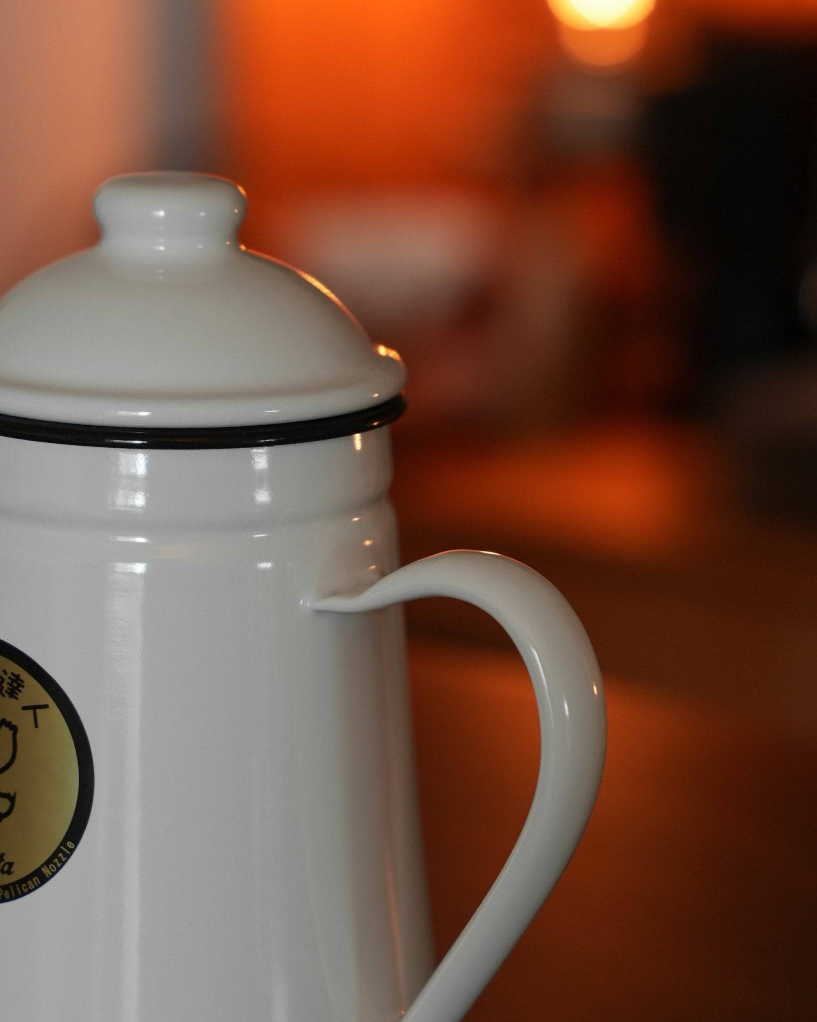 Kalita white enamel gooseneck kettle for pour-over coffee, 1L capacity, with brand logo visible, against warm orange background, showcasing elegant design and professional quality for precise brewing