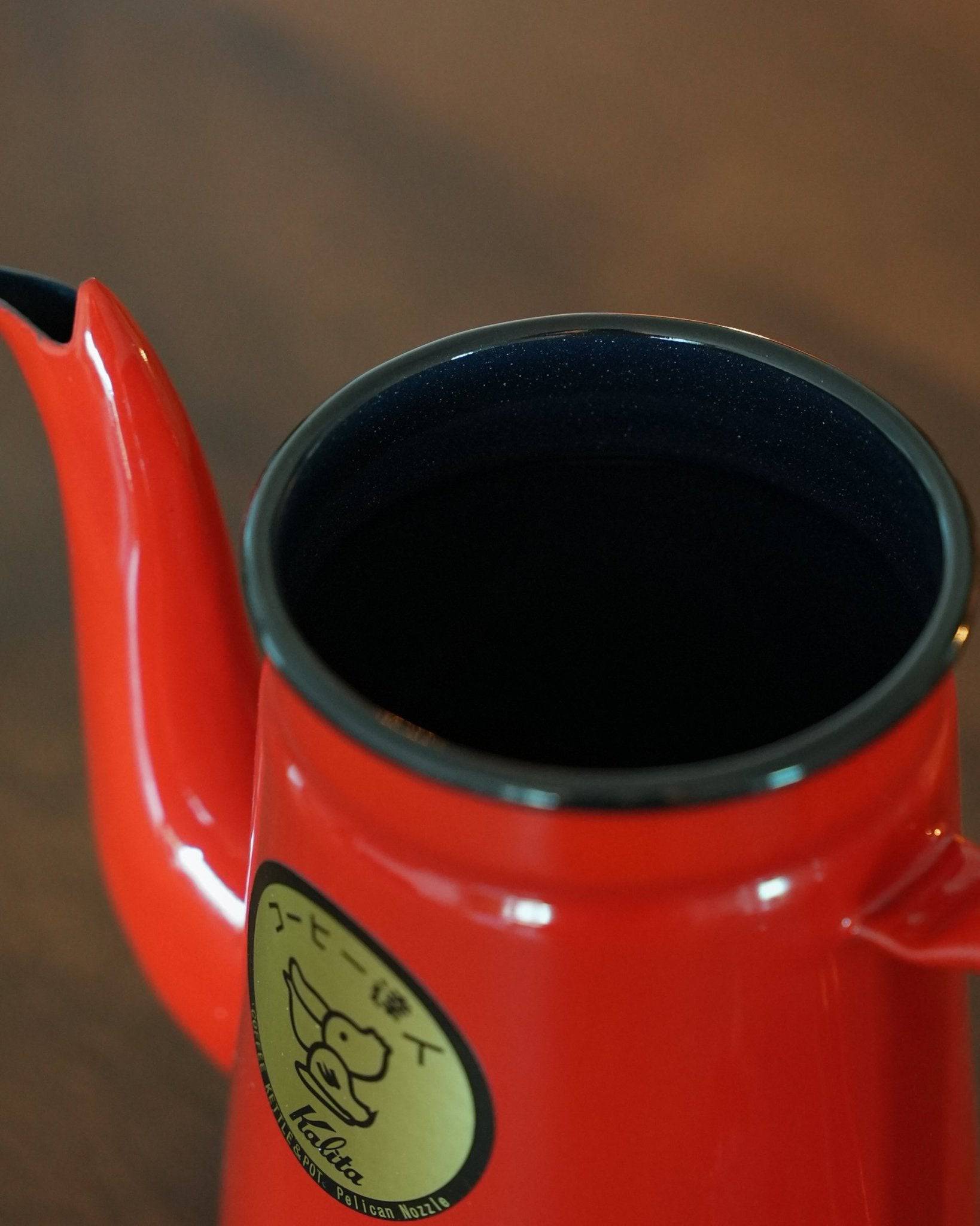 Closeup of red Kalita enamel pour-over kettle with gooseneck spout, showcasing its sleek design and gold brand logo on a wooden surface