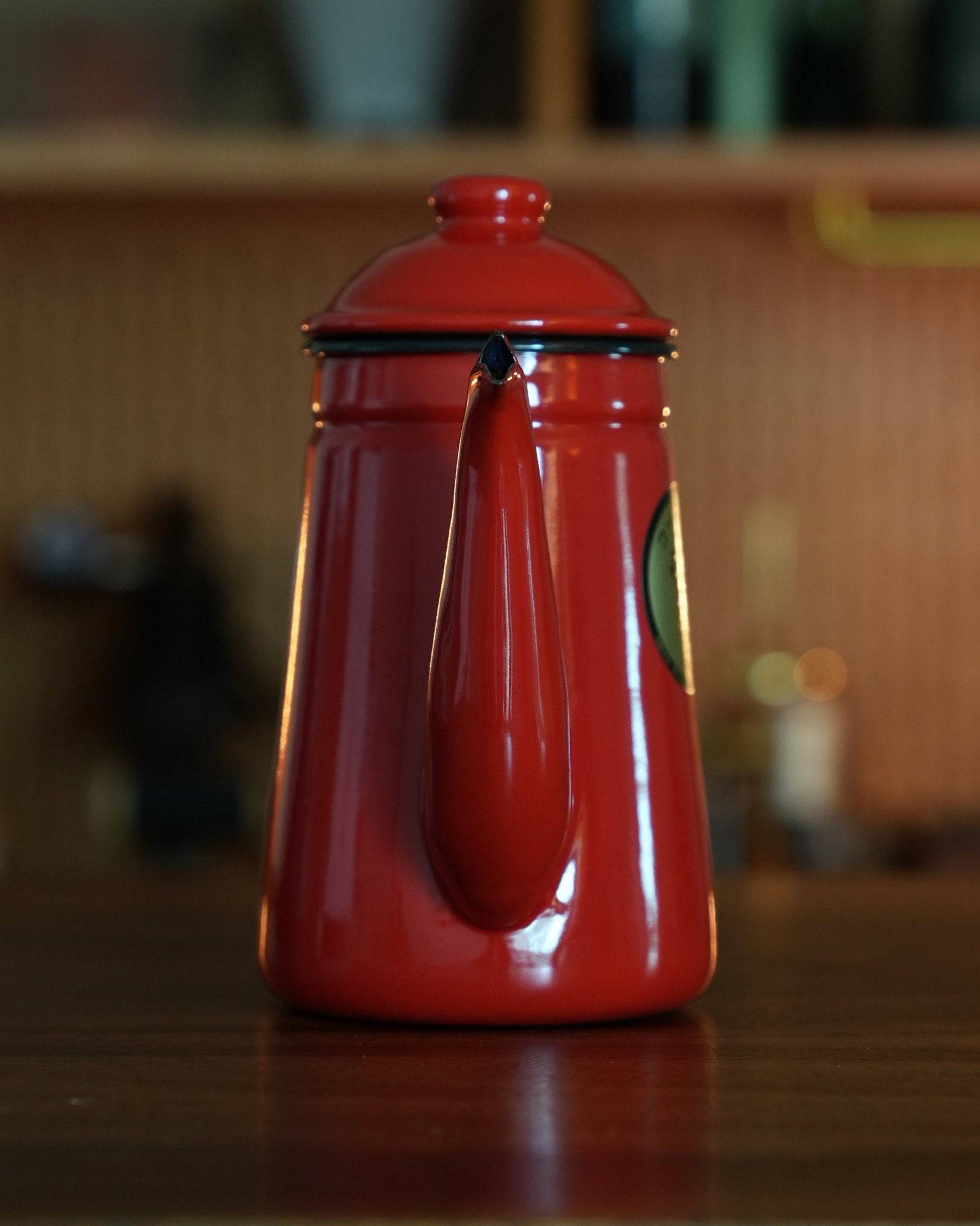 Stylish red enamel Kalita pour-over coffee kettle with gooseneck spout on wooden surface, perfect for precise brewing control and elegant kitchen decor