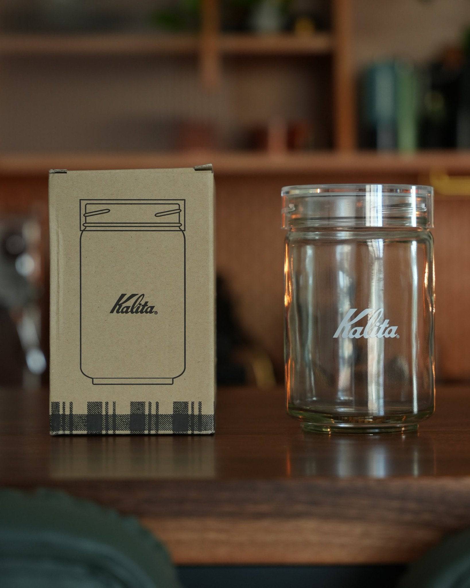 Kalita glass coffee canister with packaging box on wooden surface, showcasing transparent jar design with brand logo and airtight lid for fresh coffee storage