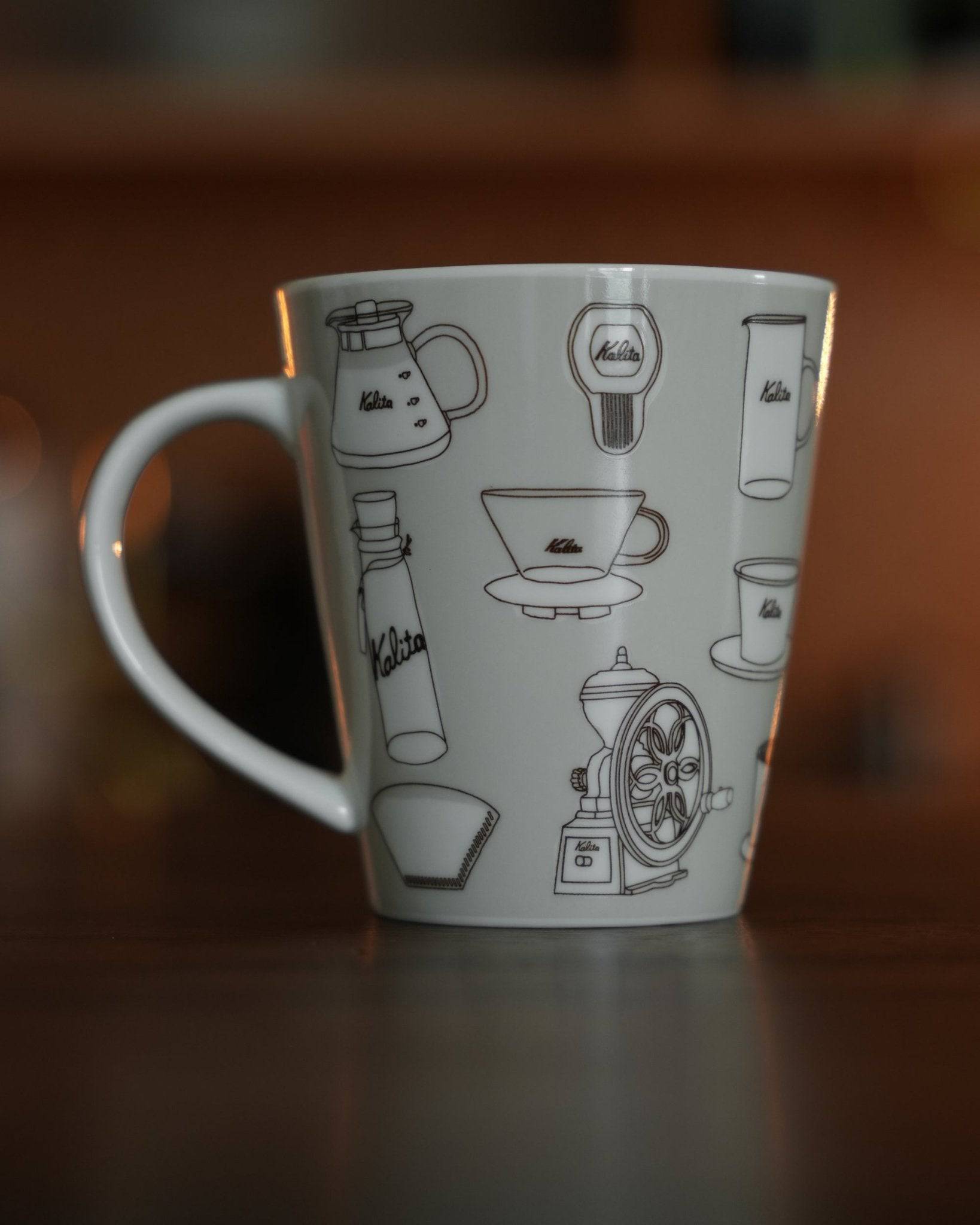 Kalita ceramic mug featuring illustrated coffee equipment designs on warm gray background, showcasing coffee pots, grinders, filters, and cups in black line art style, perfect for coffee enthusiasts and collectors