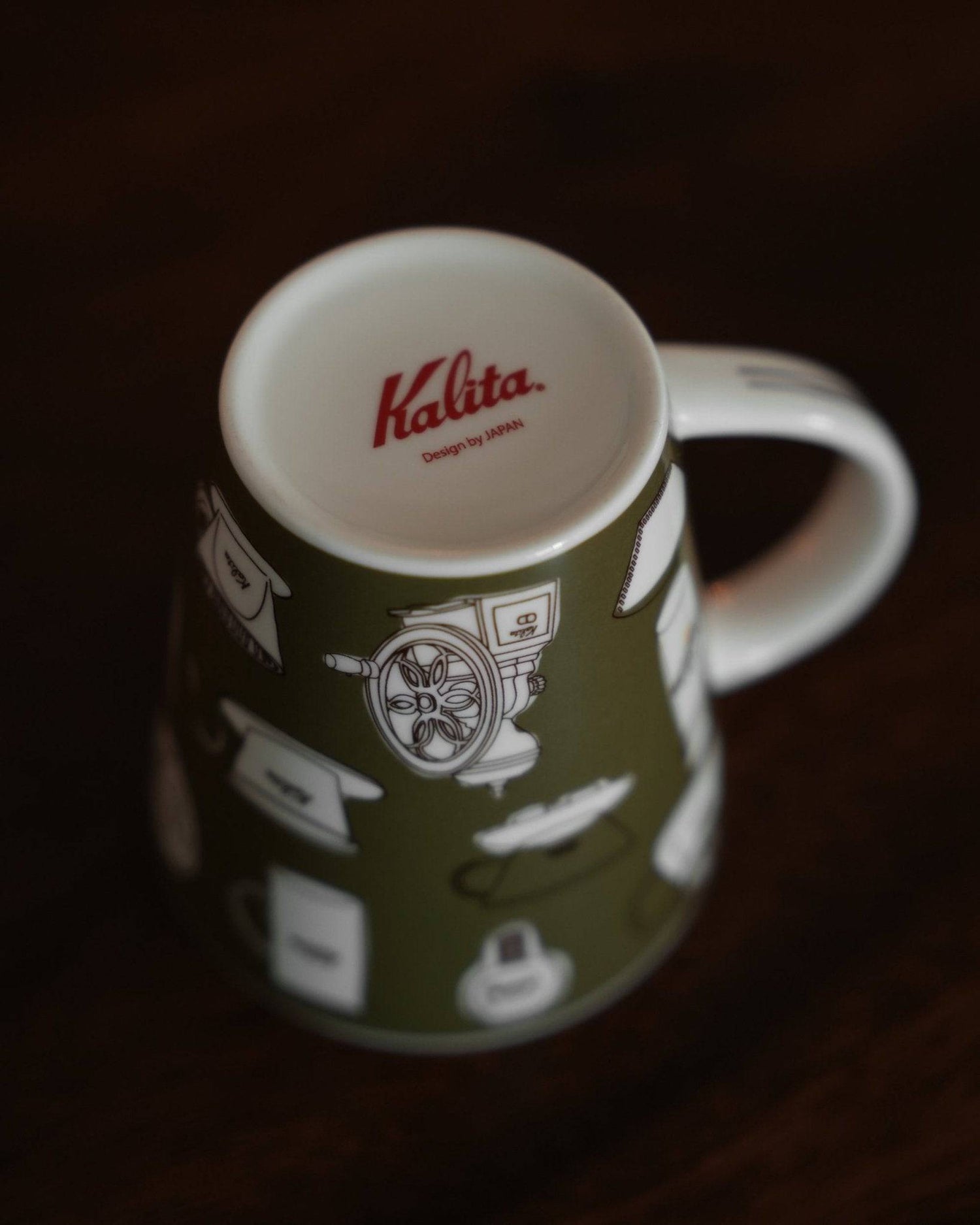 Kalita ceramic mug in khaki green with white coffee equipment illustrations, featuring red Kalita logo on inner rim, displayed on dark wooden surface