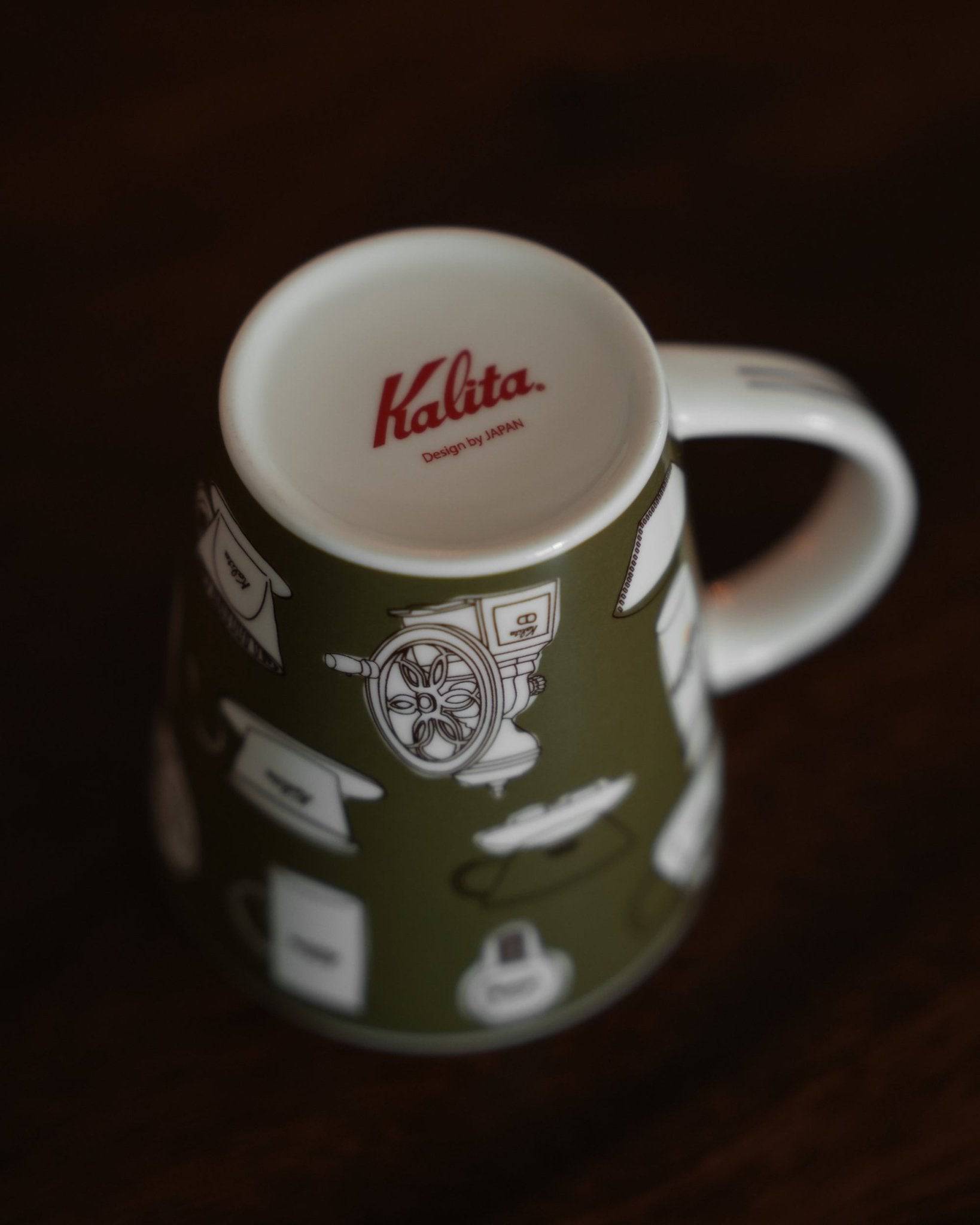 Kalita ceramic mug in khaki green with white coffee equipment illustrations, featuring red Kalita logo on inner rim, displayed on dark wooden surface