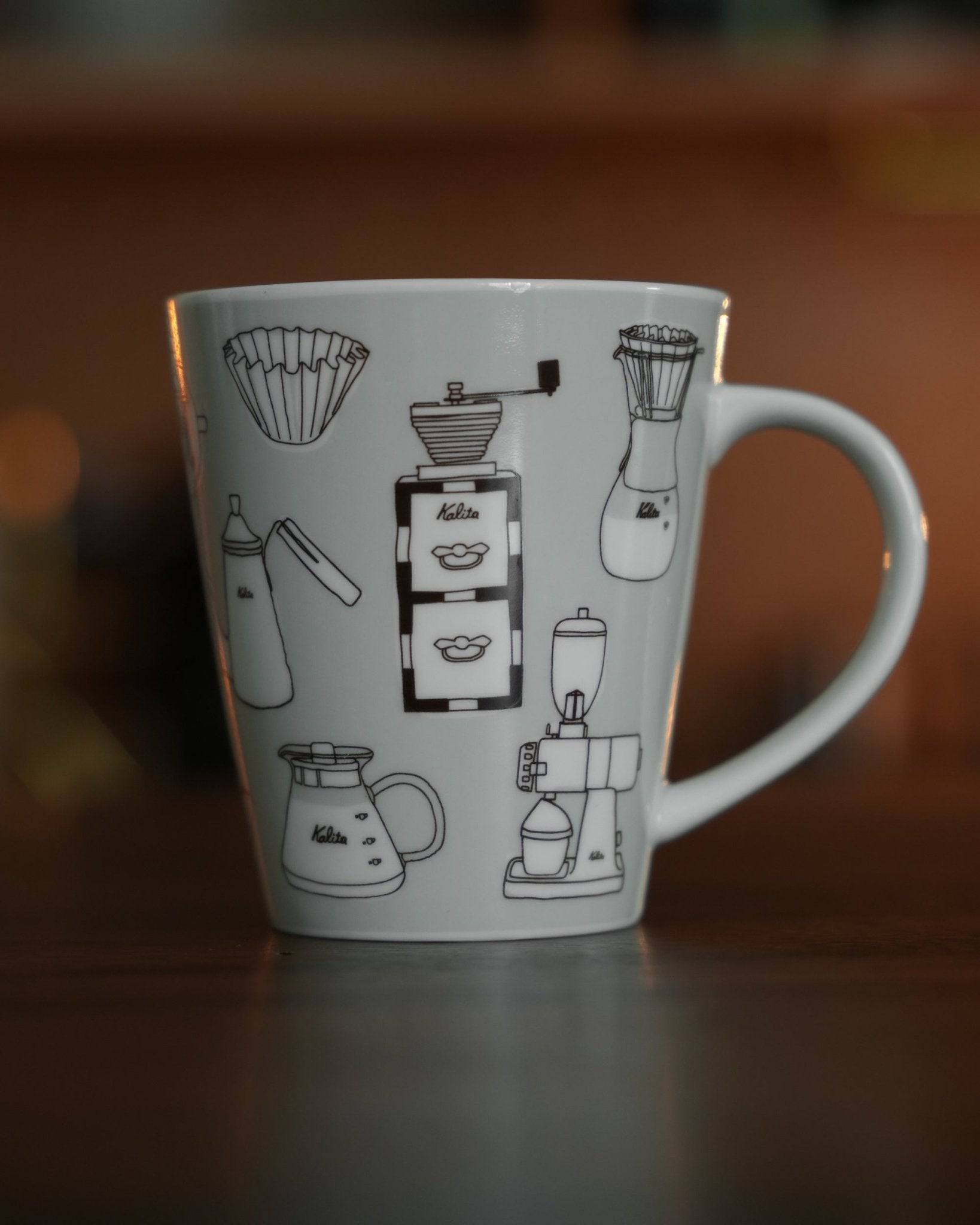 Kalita ceramic mug with coffee equipment illustrations, including grinder, kettle, filter, and brewer, on warm gray background. Stylish and collectible 300ml cup for coffee enthusiasts.