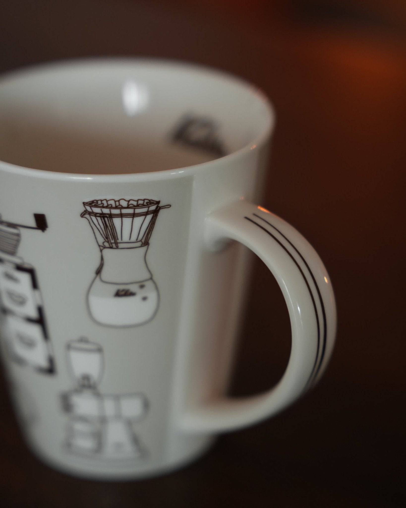 Kalita ceramic mug in warm gray, featuring black line illustrations of coffee equipment including pour-over dripper, grinder, and filter. Close-up view highlighting the mug&