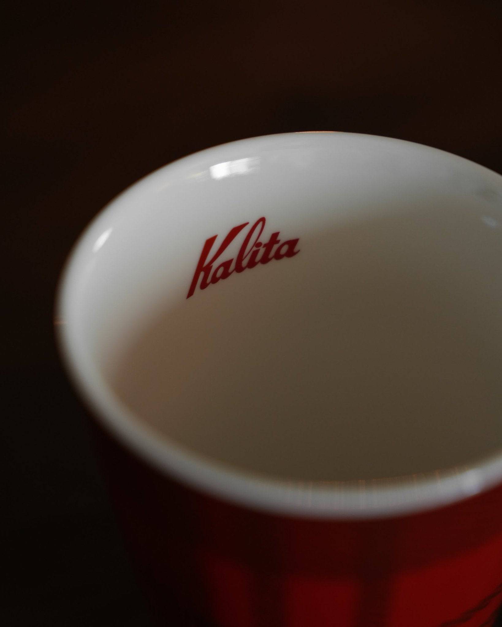 Close-up of Kalita ceramic mug, showing white interior with red Kalita logo and partial view of red exterior with checkered pattern, highlighting brand and design details of the 300ml coffee cup
