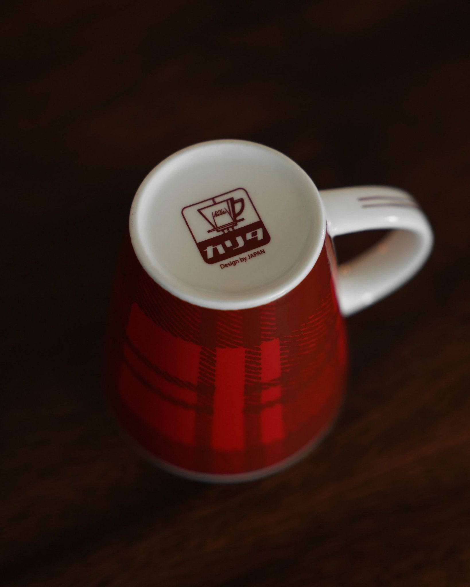 Red ceramic Kalita mug with checkered pattern, featuring white interior and Kalita logo, photographed on dark background, showcasing Japanese coffee brand&