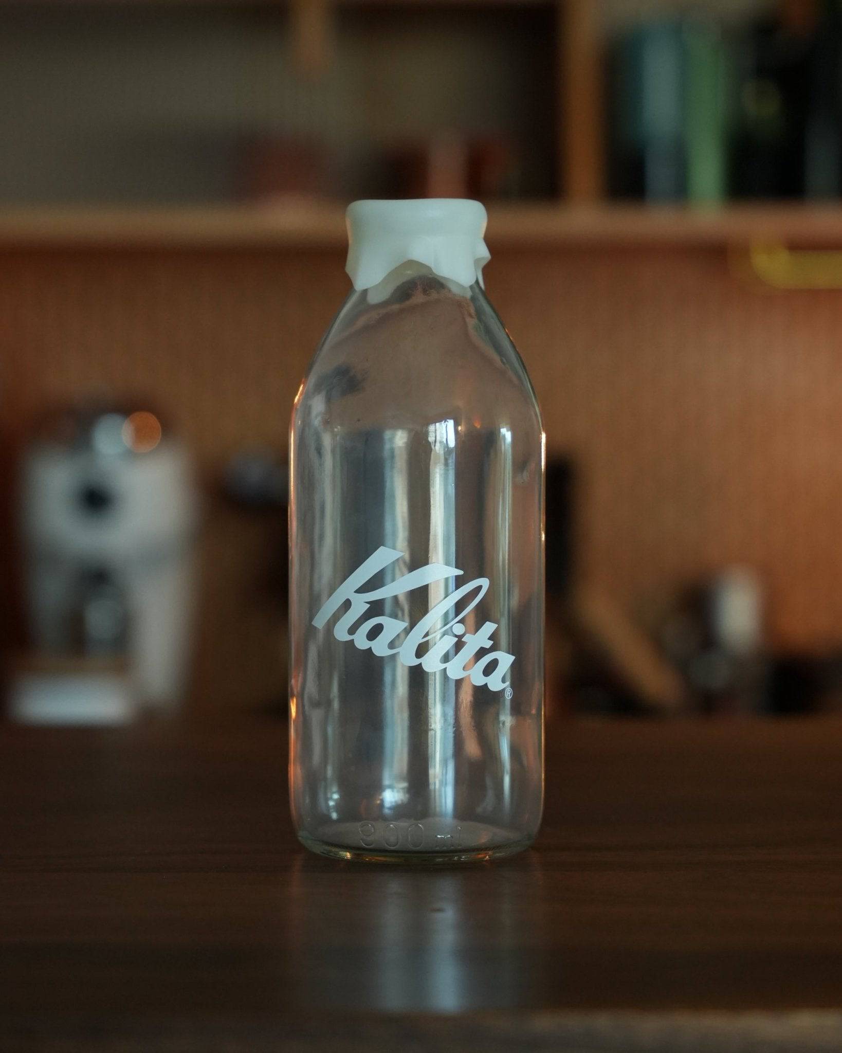 Kalita glass milk bottle shaped coffee bean storage jar 320g on wooden counter, stylish kitchen accessory with Kalita logo, transparent container with white lid
