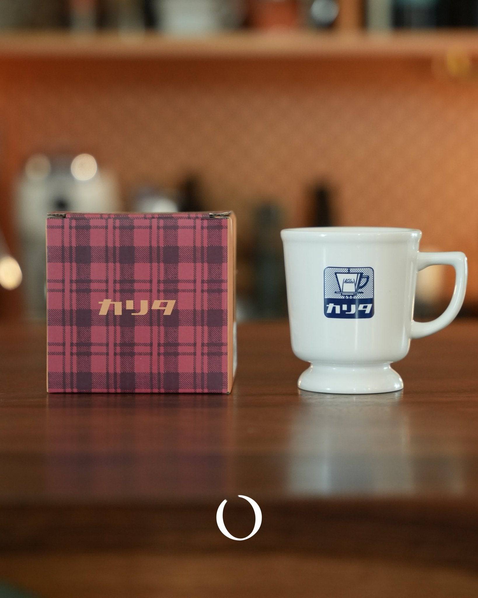 Vintage Kalita coffee mug with blue logo next to its plaid packaging box on wooden surface, evoking nostalgic Japanese cafe atmosphere