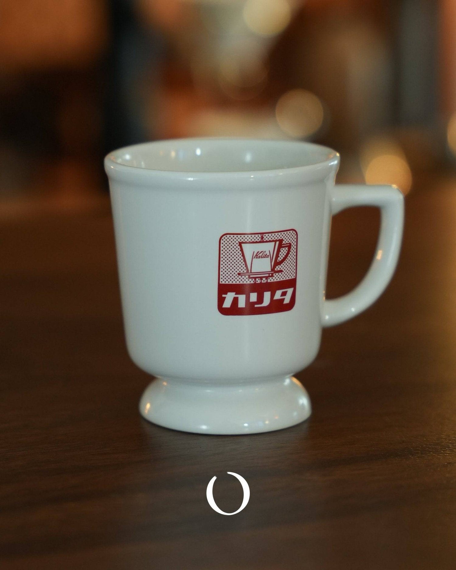 Vintage Kalita coffee mug with red logo, white ceramic, retro Showa era design, wide mouth and elevated base, on wooden table with blurred background