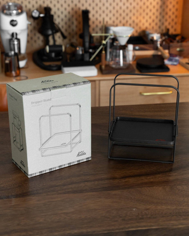 Kalita adjustable coffee dripper stand with product box on wooden table, surrounded by coffee brewing equipment in background