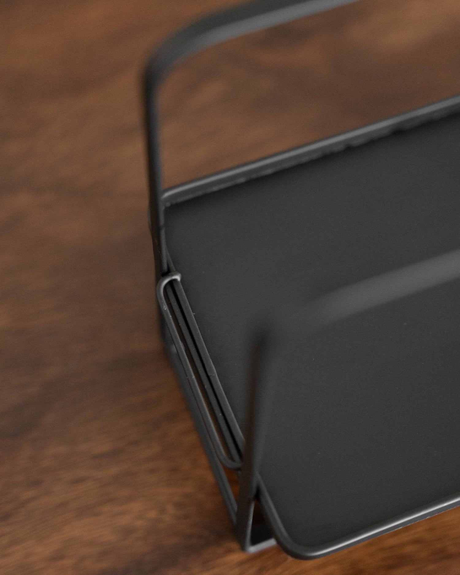 Close-up view of Kalita adjustable coffee dripper stand, showing sleek black metal design with curved edges and sturdy construction on wooden surface, highlighting its functionality and aesthetic appeal for pour-over coffee brewing