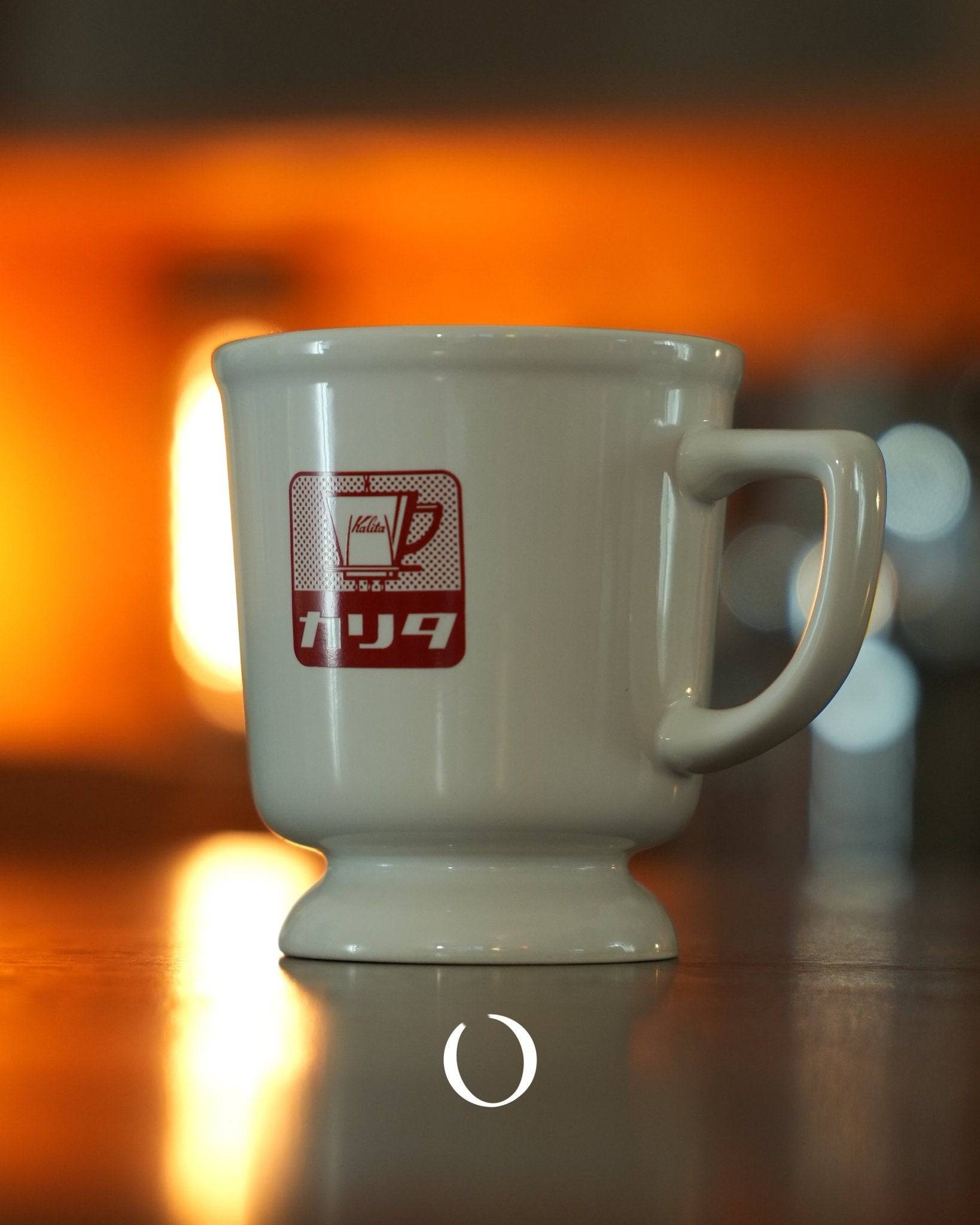 Kalita retro coffee mug in white ceramic with red logo, showcasing Showa era design, against warm orange background, reflecting nostalgic Japanese coffee culture