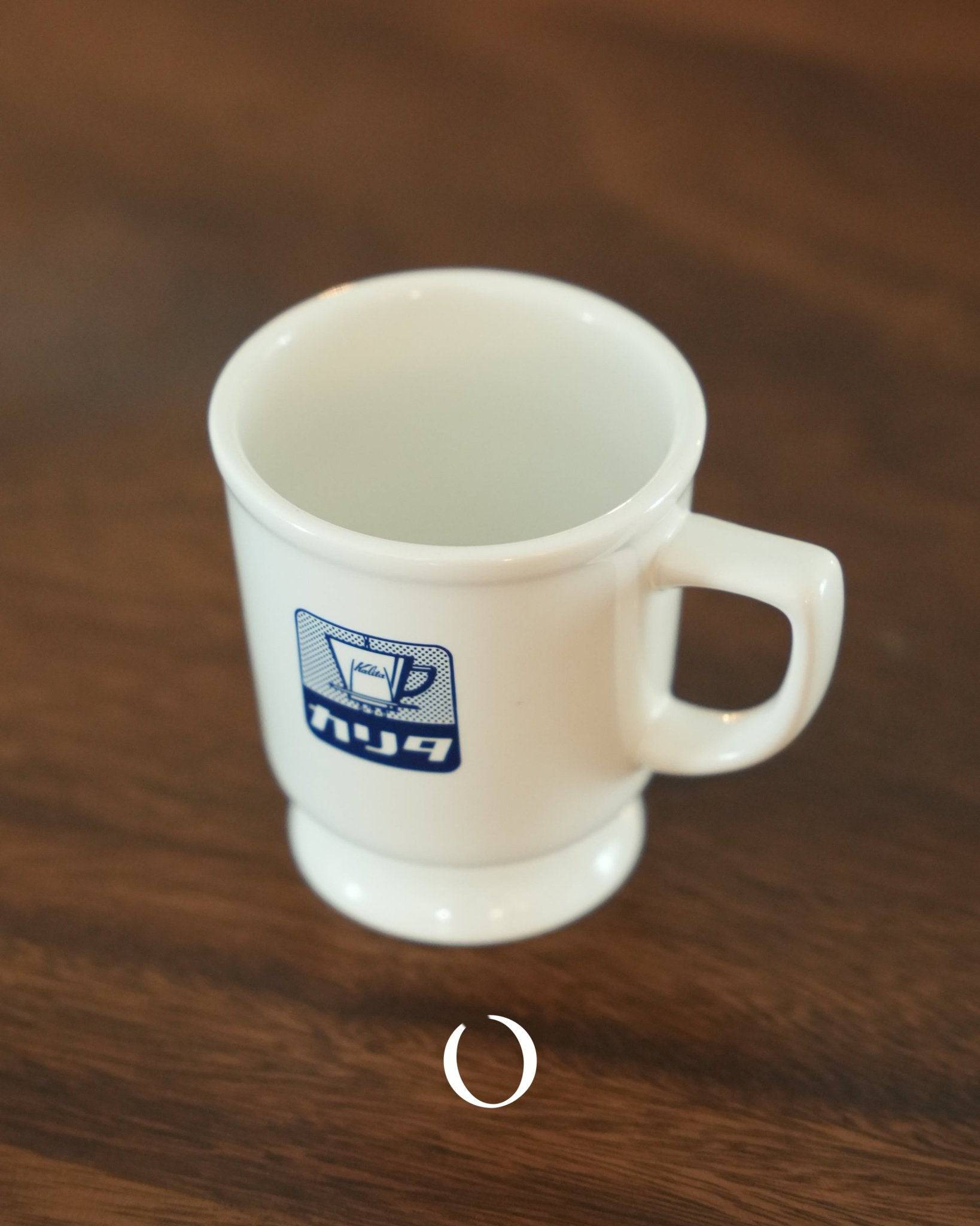 Kalita retro coffee mug in white ceramic with blue logo, featuring thick walls and wide rim, placed on wooden surface, embodying Showa era design for nostalgic cafe experience at home