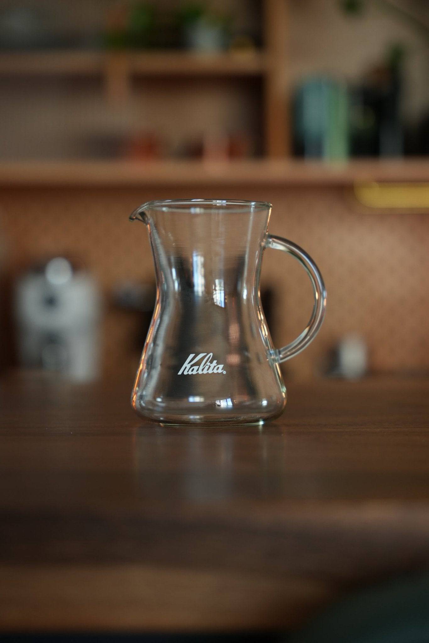 Kalita conical server 300 glass coffee carafe on wooden table in kitchen setting, showcasing heat-resistant design and Kalita logo