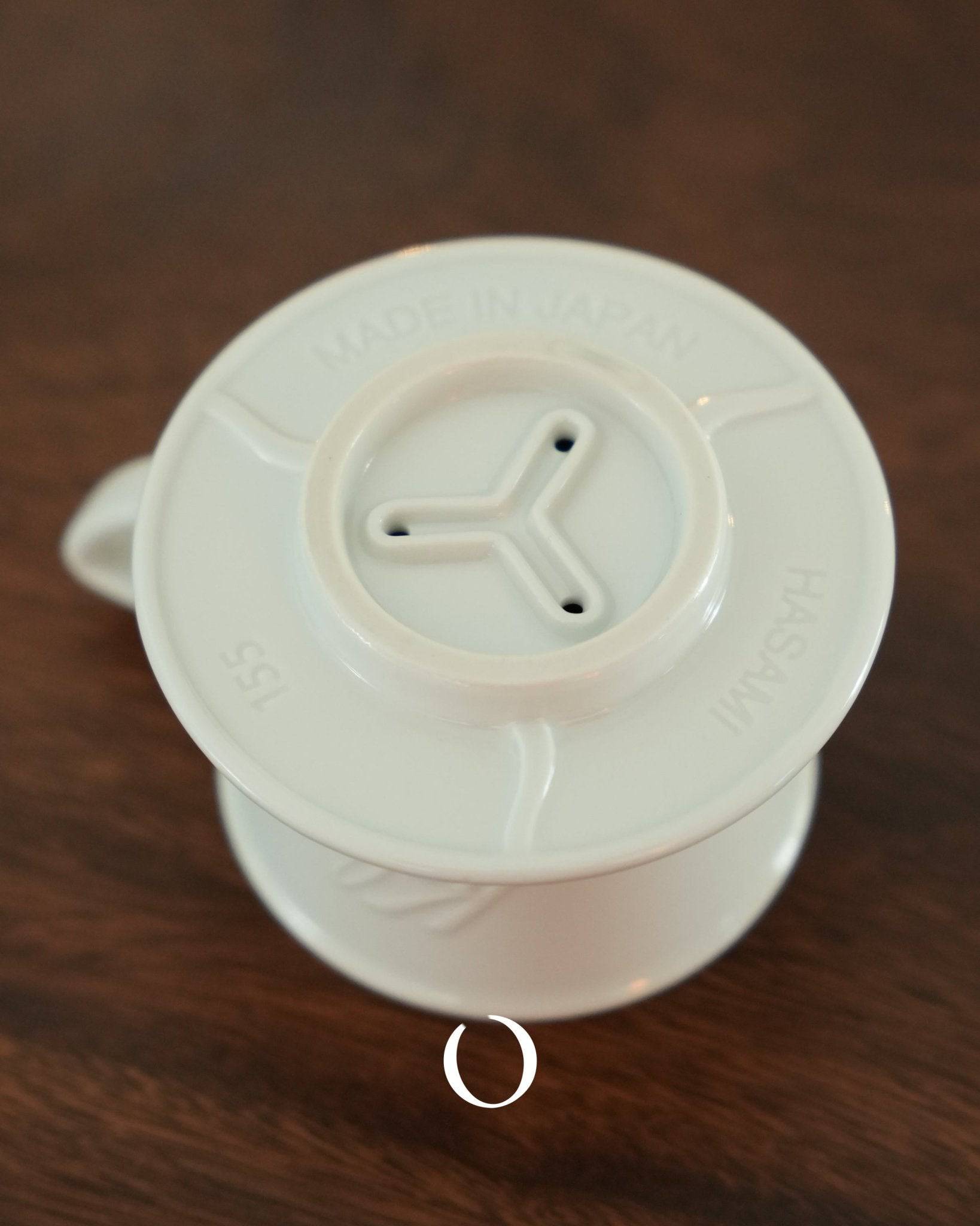 KALITA & HASAMI ceramic coffee dripper with three-hole design, showcasing traditional Hasami-yaki craftsmanship. White porcelain pour-over cone on wooden surface, highlighting its elegant shape and practical functionality for brewing perfect coffee.